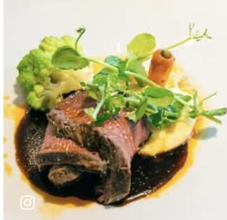 Plate with cooked beef, mashed potatoes, broccoli, and a carrot with greens, garnished with herbs and sauce