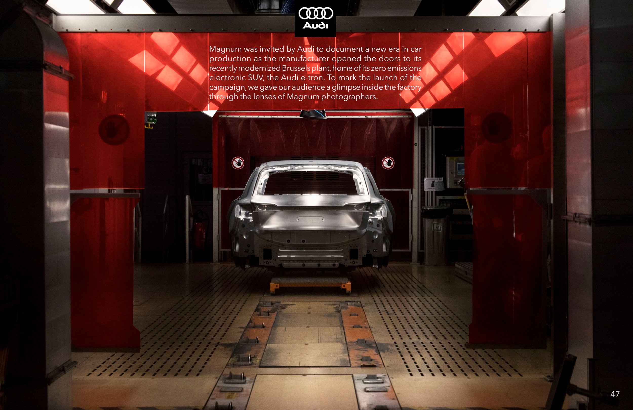 Photo of an automotive manufacturing plant with a silver car body shell on an assembly line, surrounded by red fixtures and machinery, and a sign about Audi.