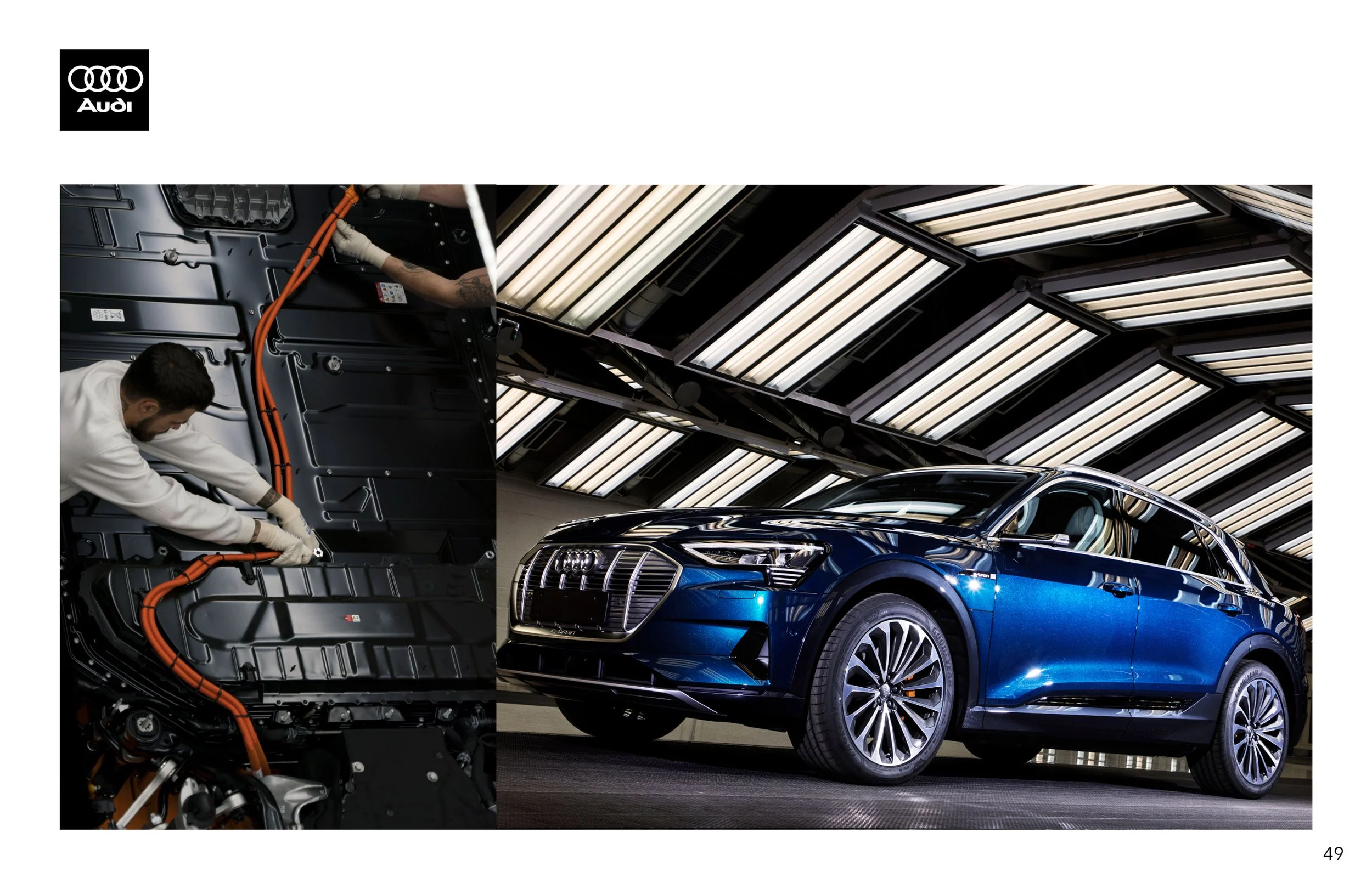 A blue Audi car parked indoors with its hood open, showing two mechanics working on the engine. The setting has bright overhead lighting and a modern design ceiling.