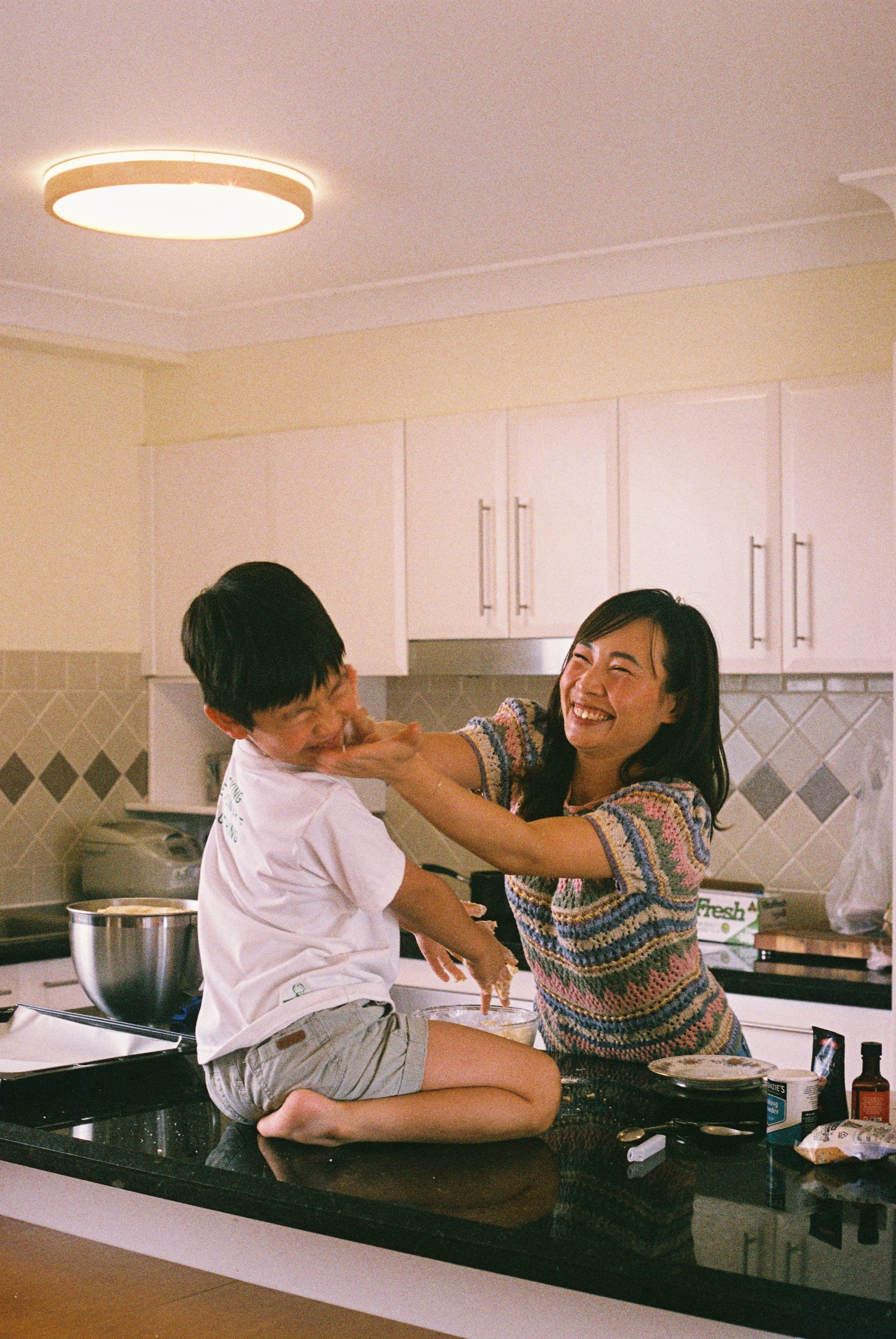 Mum cupping her son's face in her hands as he sits on the kitchen counter