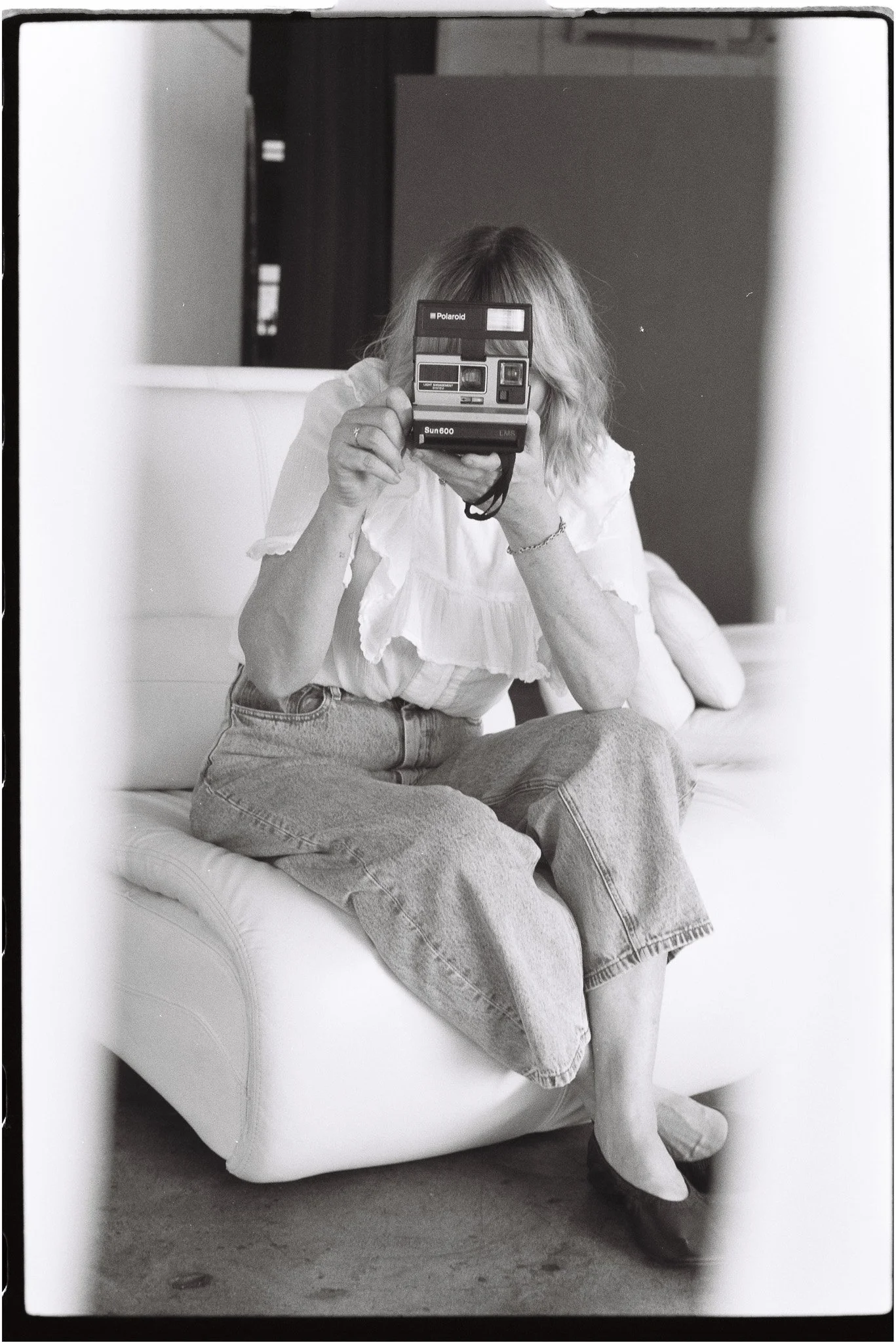 Woman seated on a chair pointing a polaroid camera at a mirror