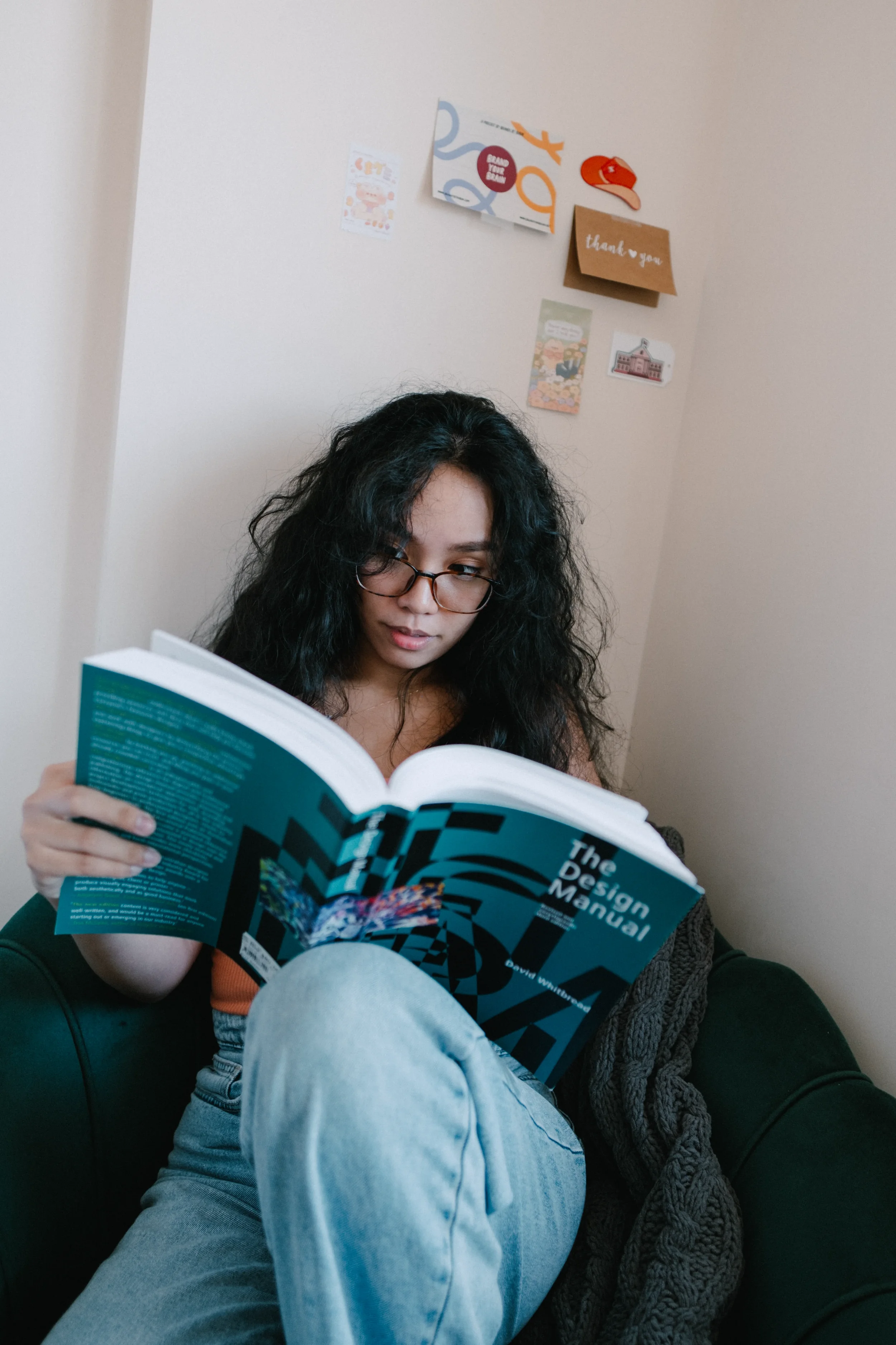 CK, Brand Designer, seated in the corner of a room with a design manual open in her lap