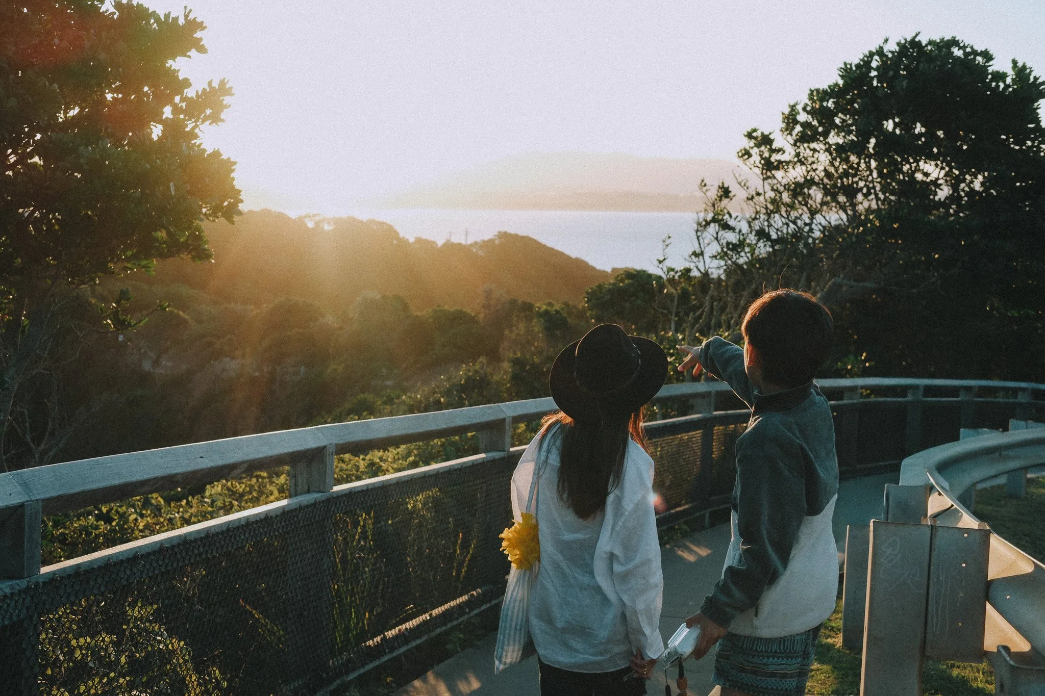 Mum and son on a mountain footpath, forest and river spread out beyond them, warm sunset light behind