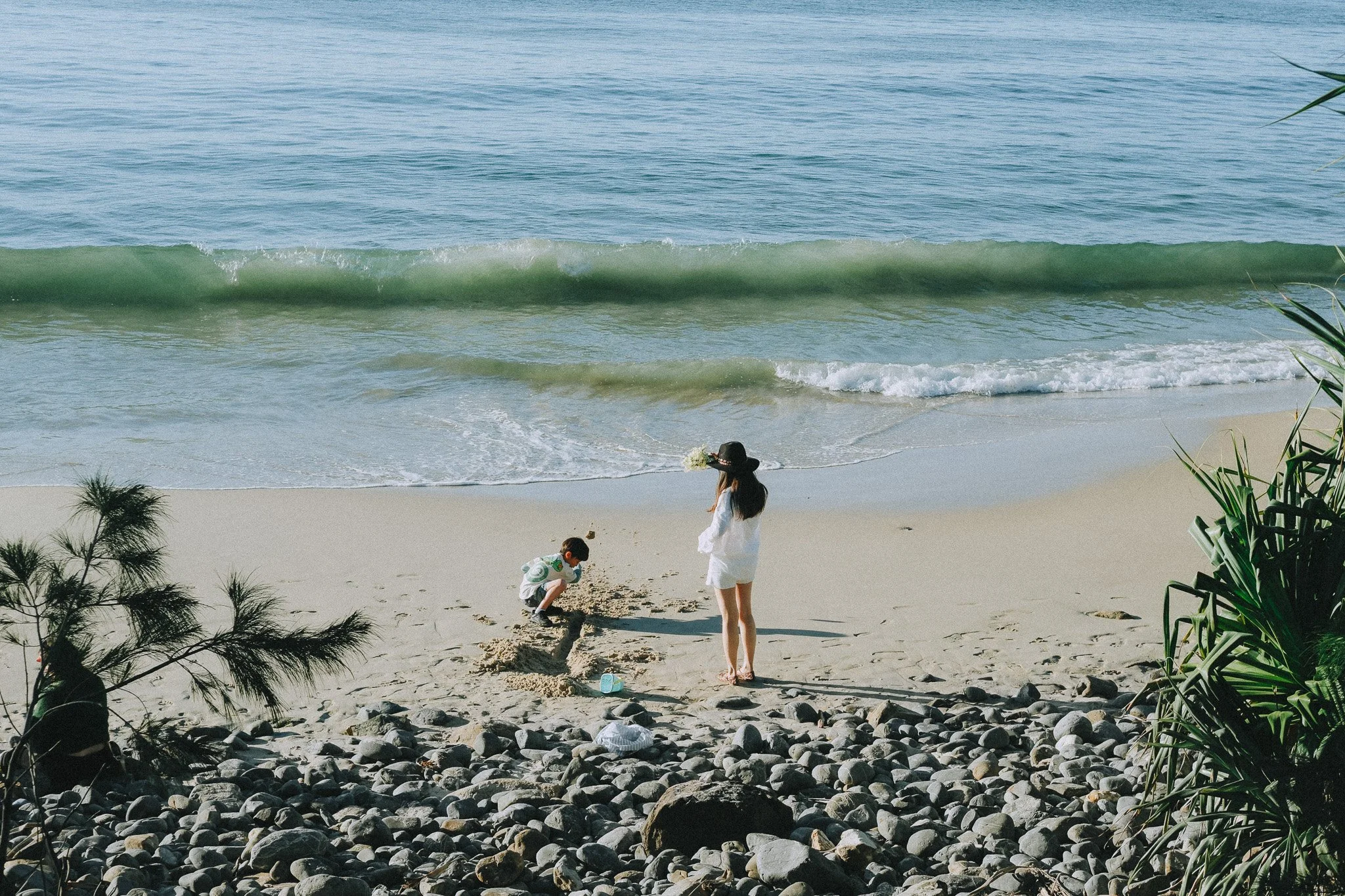 Wide shot of Mum and son on the shoreline, blue ocean behind them