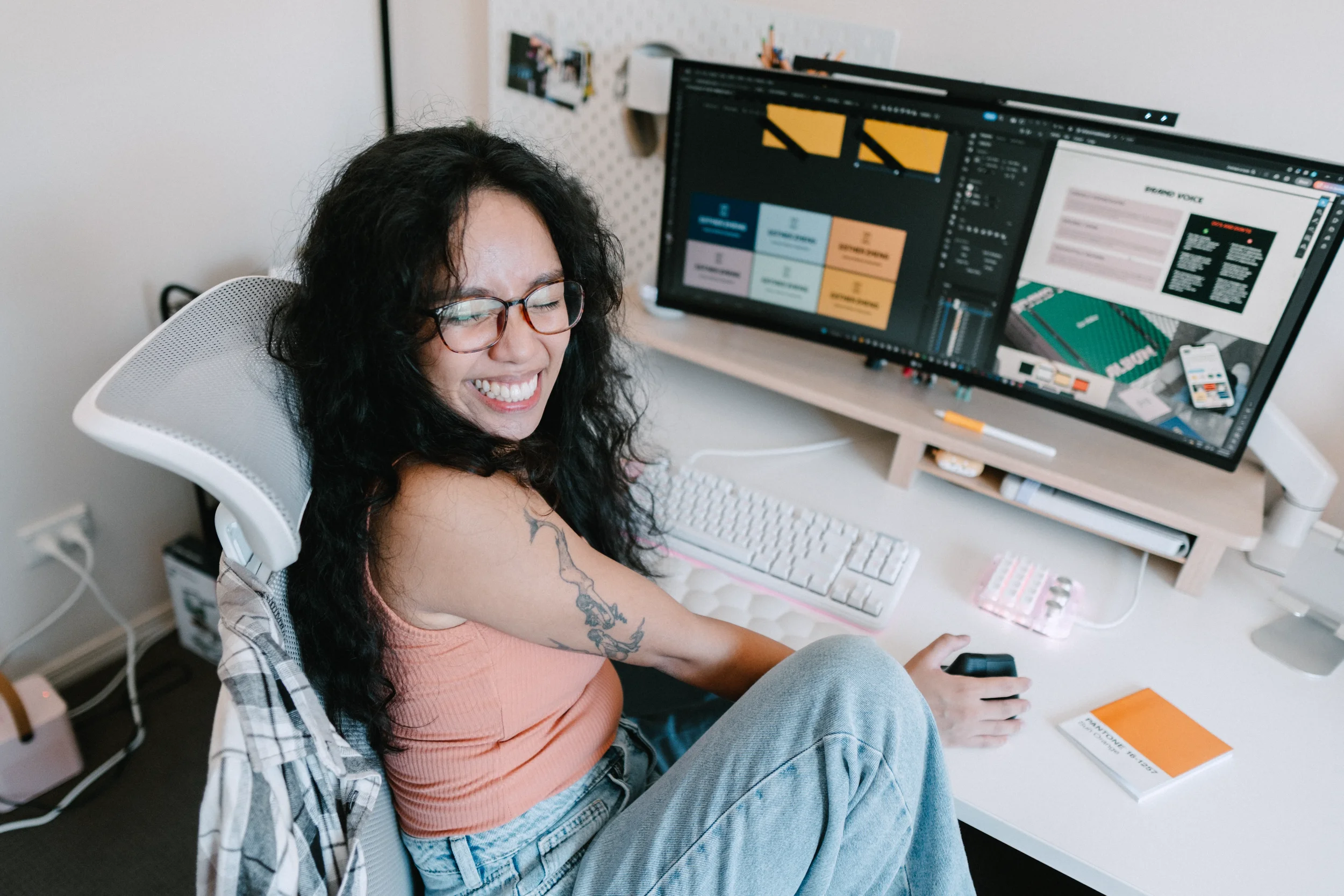 CK, Brand Designer, at her desk smiling up at the camera, design files open on screen behind her