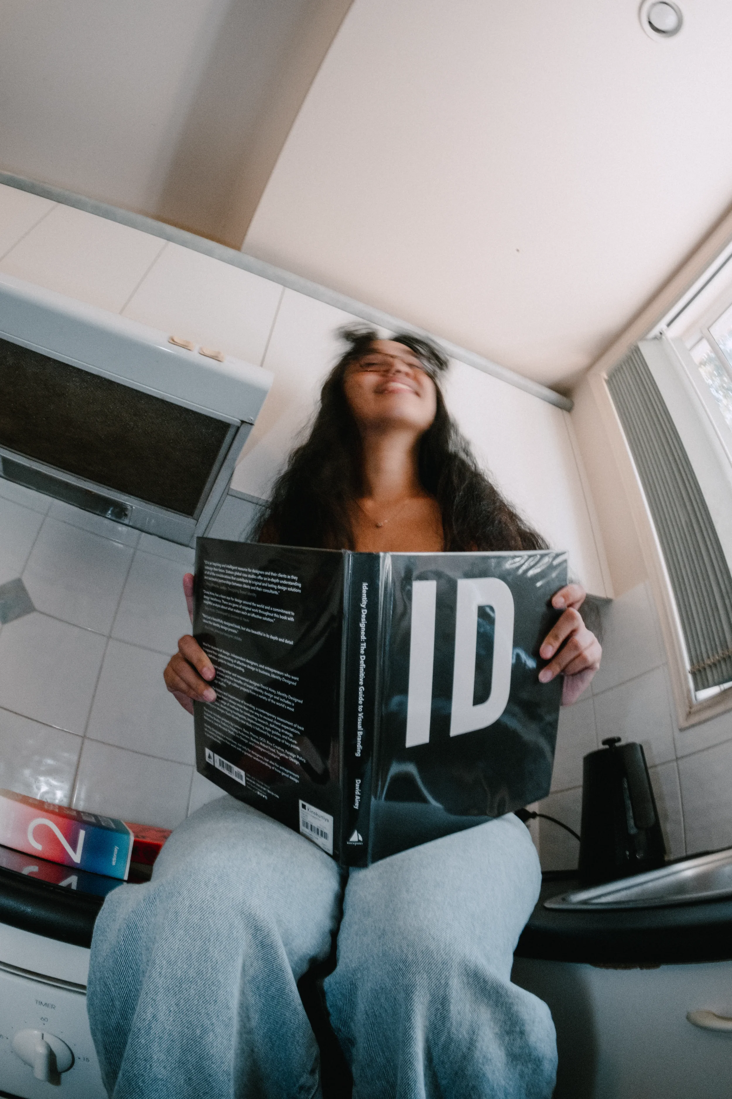 CK, Brand Designer, seated on a kitchen bench with a brand identity book open on her lap