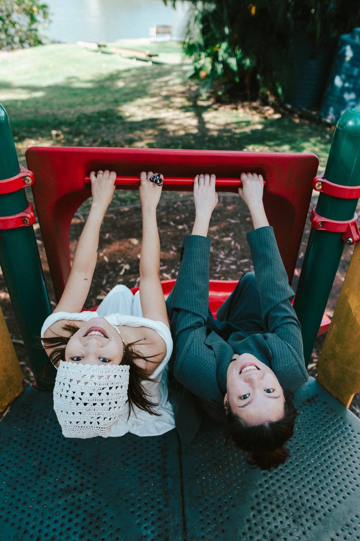 Couple leaning back against the rail of a playground slide, both looking up toward the camera