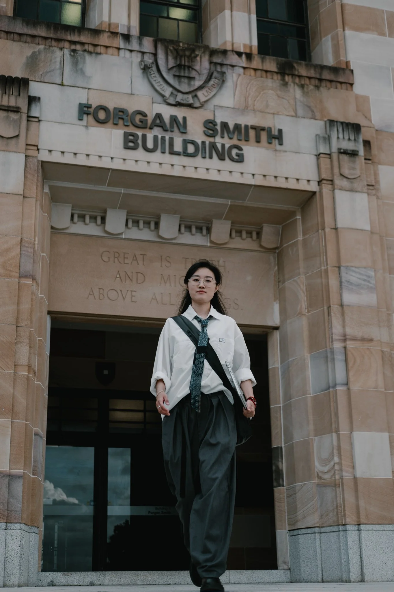 Graduate walking out through the sandstone entrance of a University of Queensland building