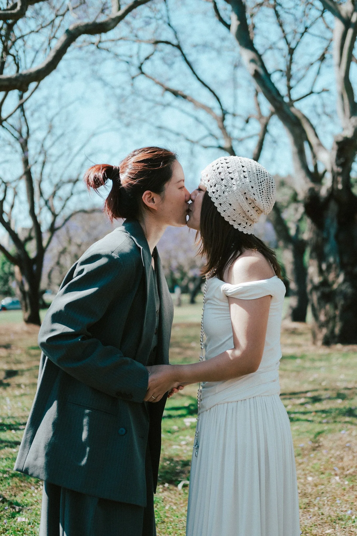 Couple kissing and holding hands in open parkland, bright afternoon sunlight