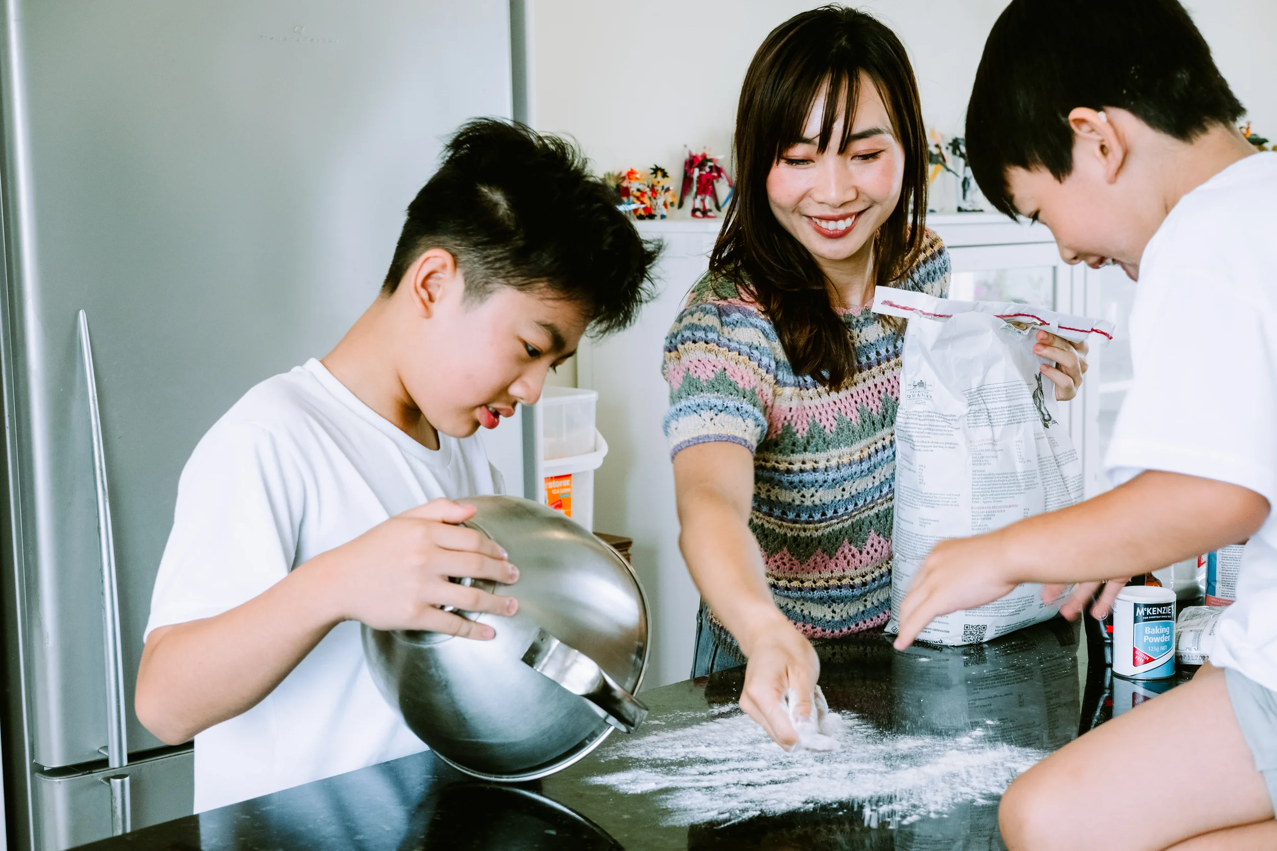 Mum and two sons baking together in the kitchen, flour spread across the counter, in bright natural light