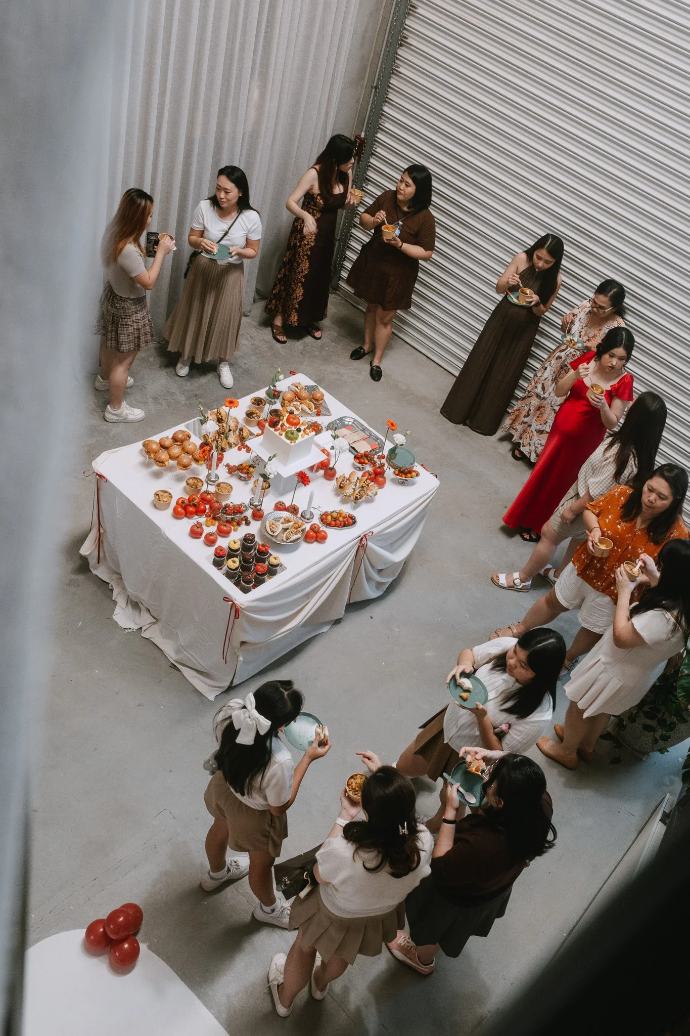 Baby shower guests surrounding a table of red and tomato-themed food, talking with each other