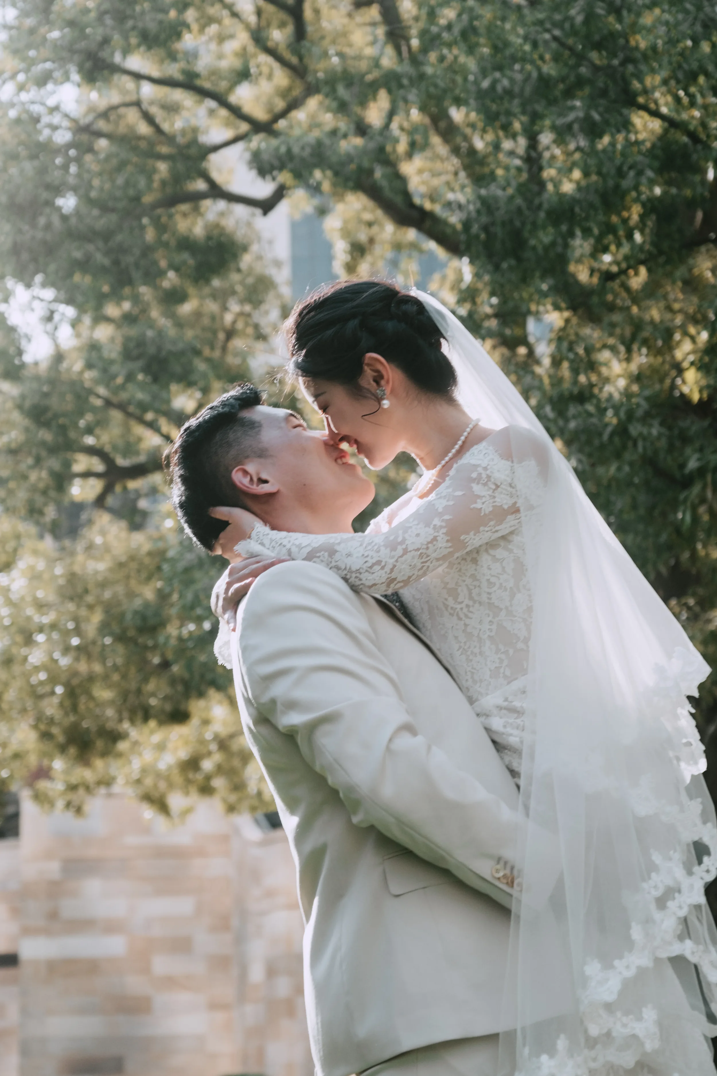 One partner lifting the other mid-kiss, morning natural light shining through the trees behind them