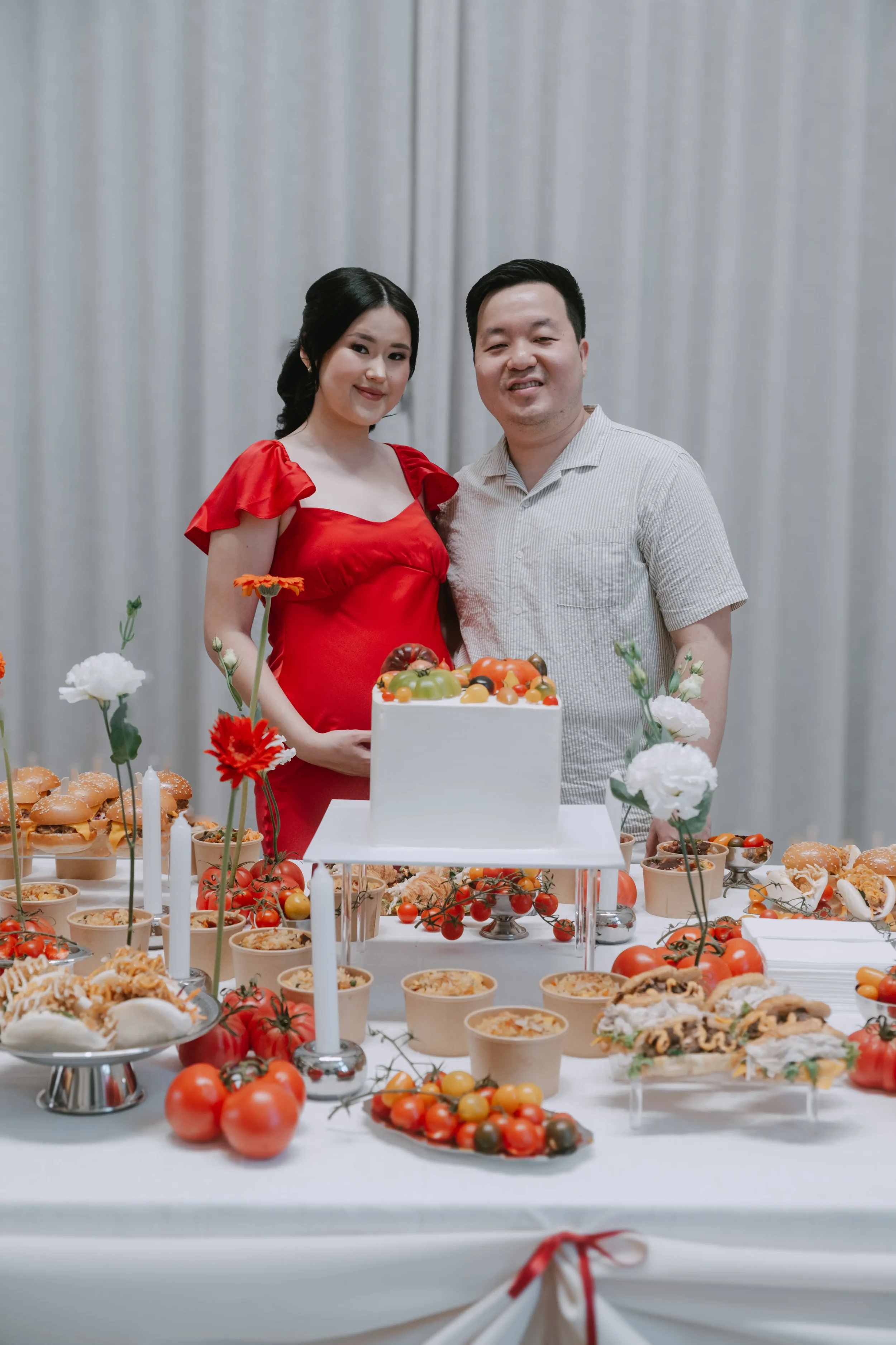 Parents-to-be standing side by side in front of a red and tomato-themed party table