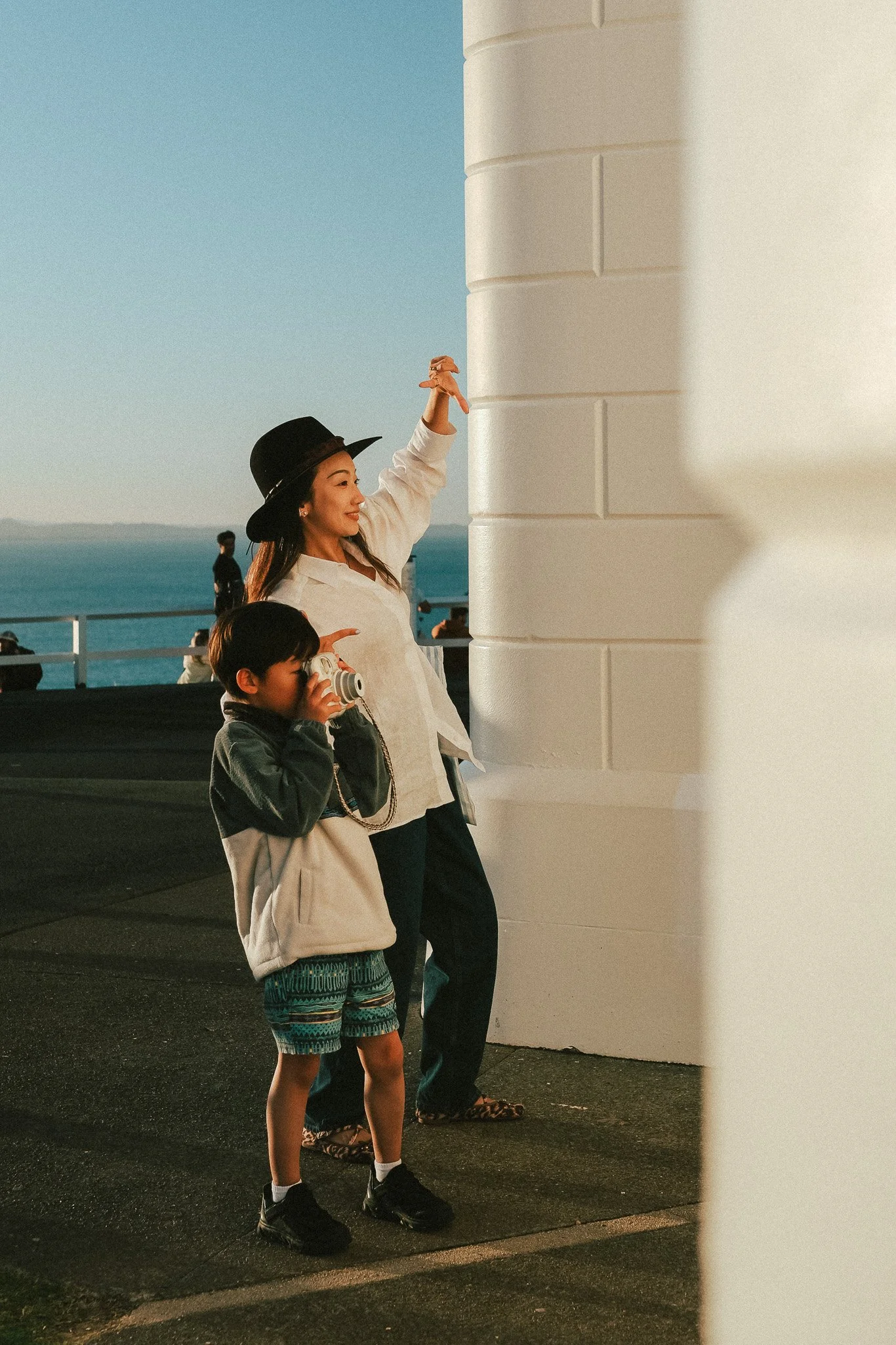 Mum and son side by side at a mountain lookout, son photographing the view on his Fujifilm Instax