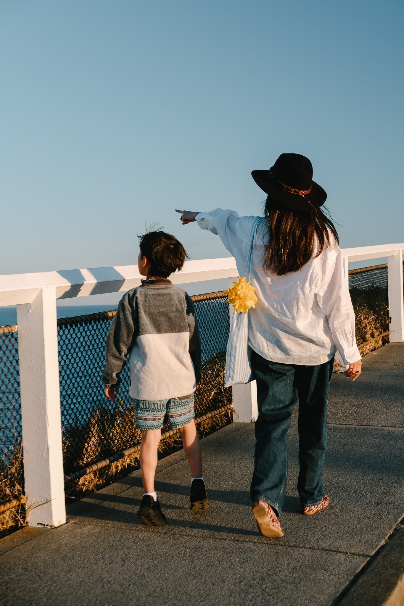 Mum and son walking side by side along a footpath, looking out over the ocean view