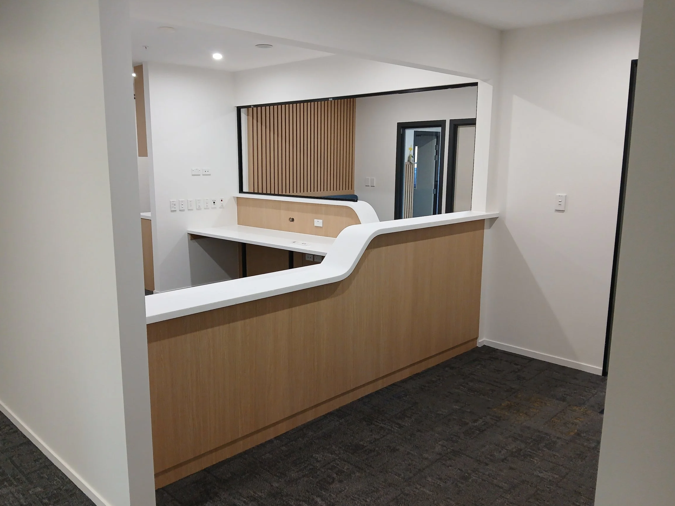 Inside view of a modern office and reception area with a white benchtop with a curve, professional workspace and office. Timber paneling on the sides.