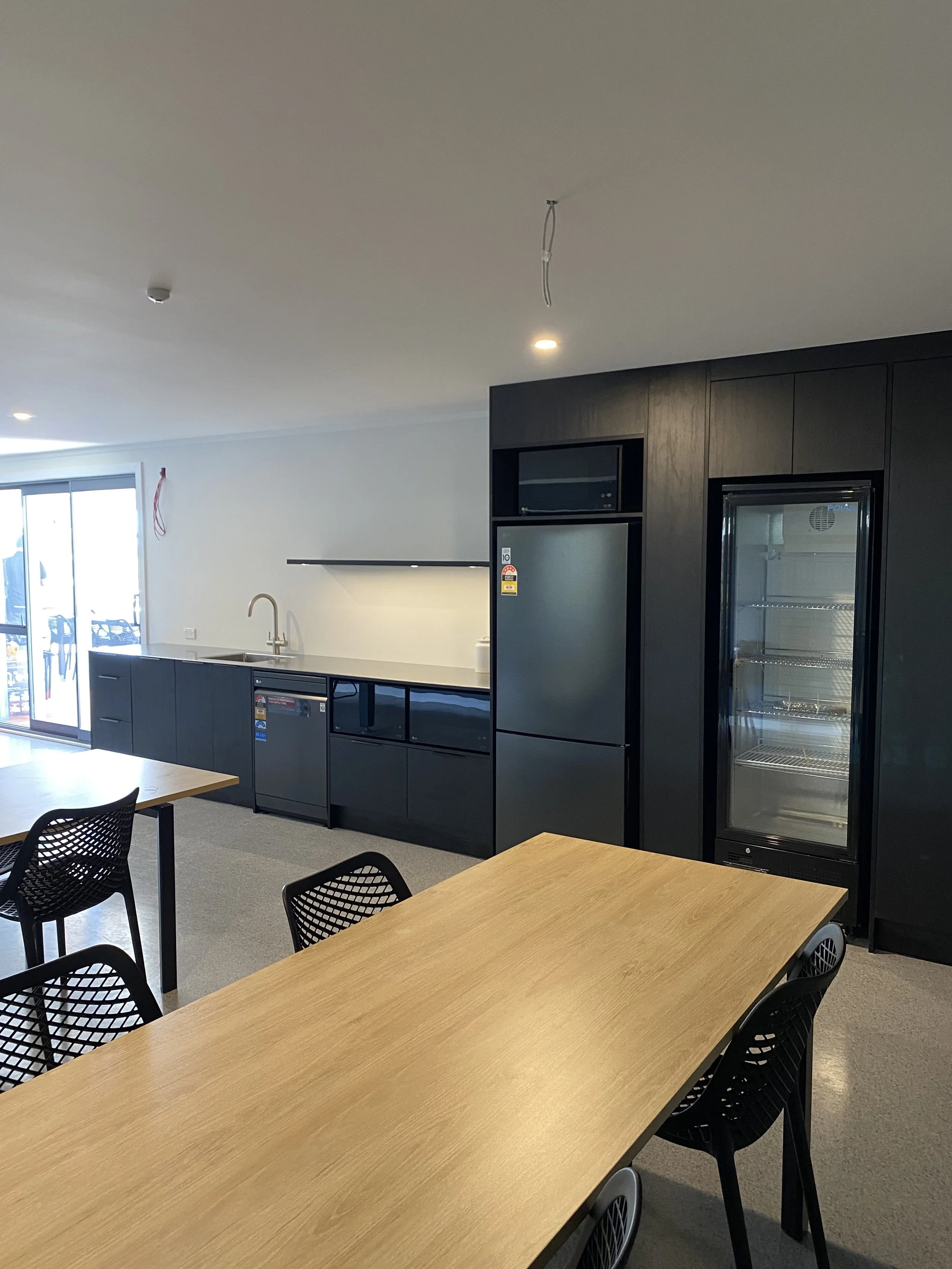 Modern staff kitchen with black cabinets, refrigerator, microwave, and a dining table with black chairs.