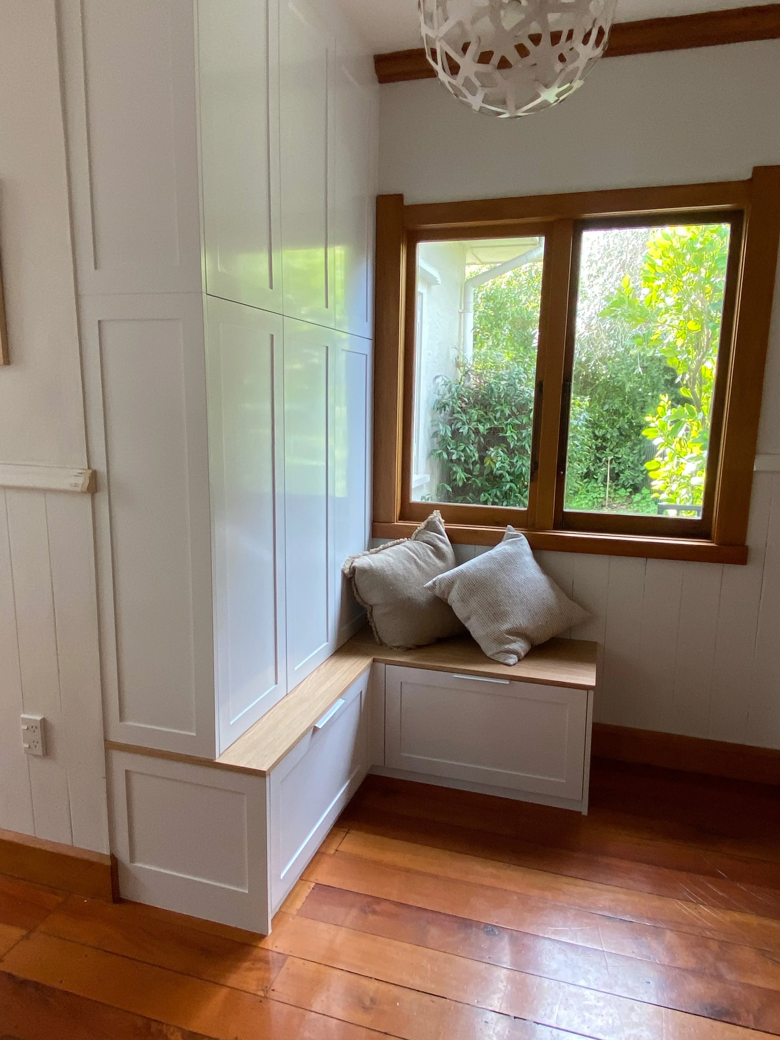 Cozy entrance way unit with built-in white wooden cabinetry and window seat with cushions. Maximising storage solutions for school bags and other home items.