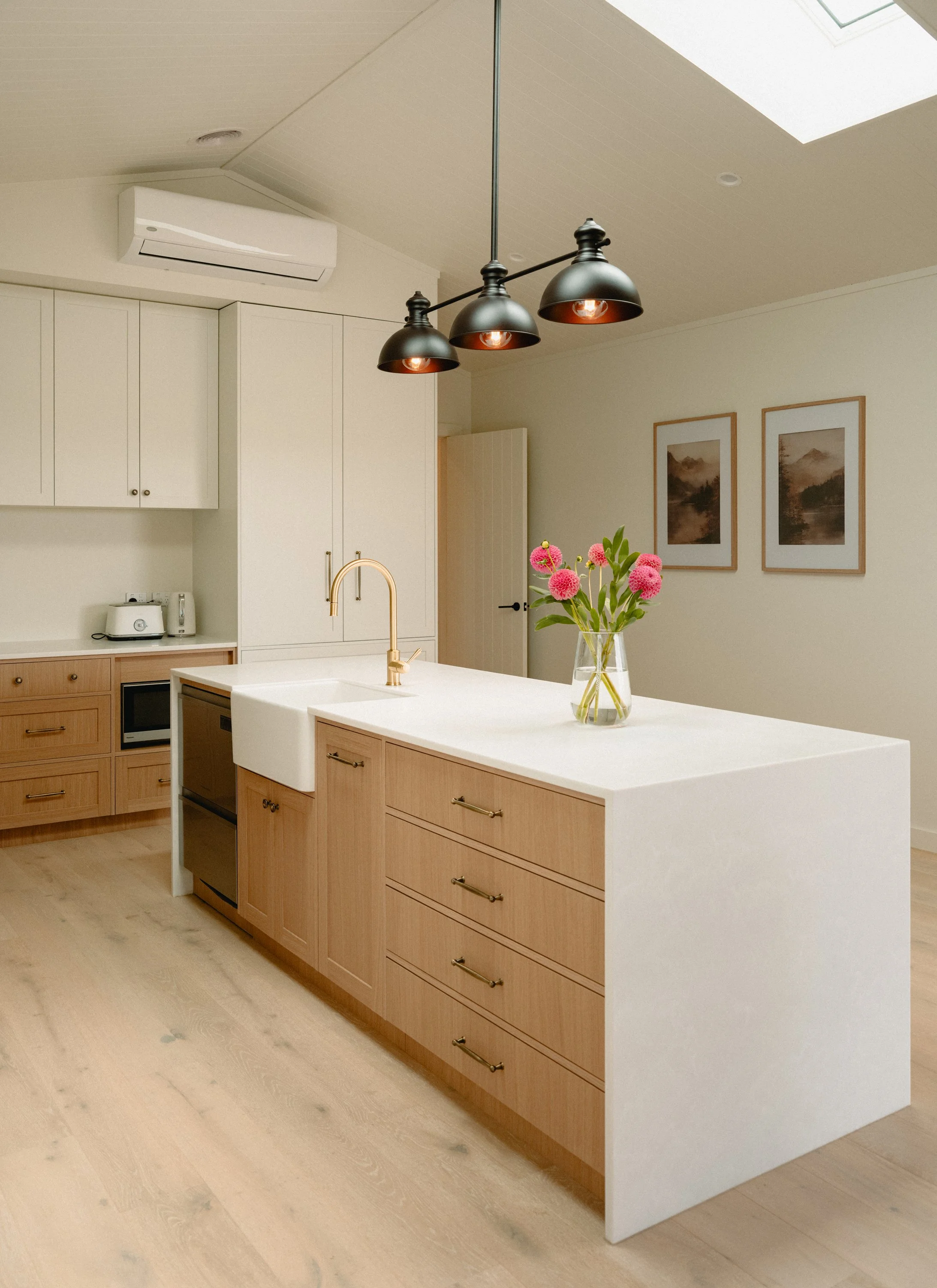 Modern kitchen with an island countertop, a vase with pink flowers, black bar stools, and white cabinets.