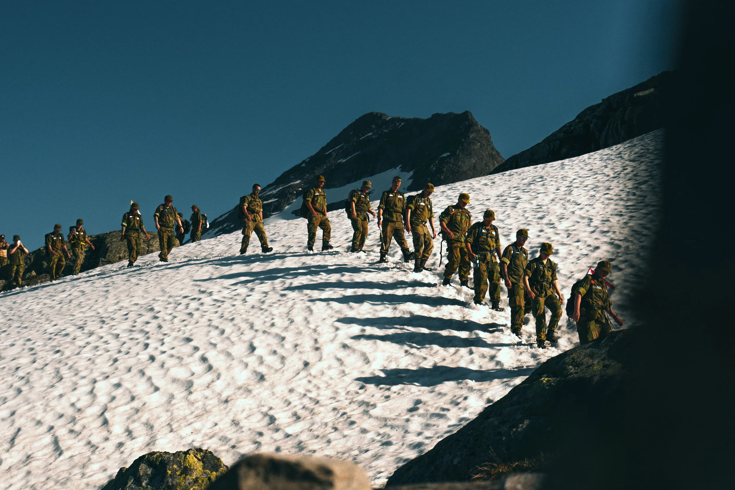 En gjeng mennesker går over et område med snø på fjellet, iført militæruniformer.