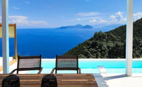 Sea view from a balcony with outdoor chairs, overlooking the ocean and distant mountains.