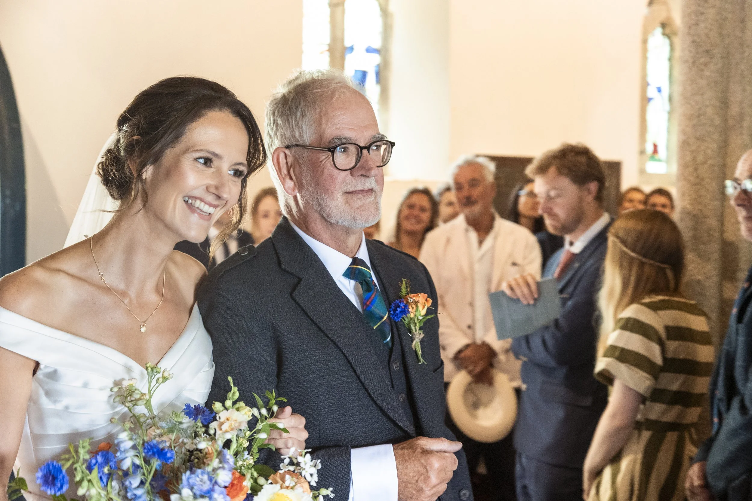 Bride and groom smiling during their wedding ceremony, with guests in the background.