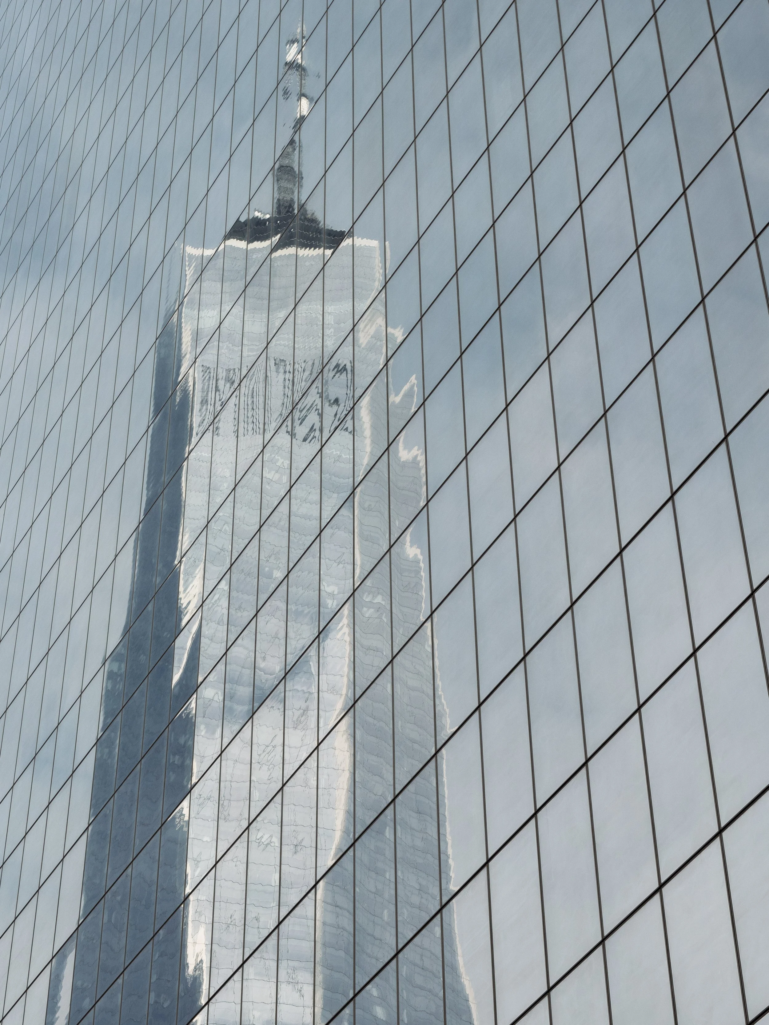 Reflection of a skyscraper with a spire in the glass windows of another building.