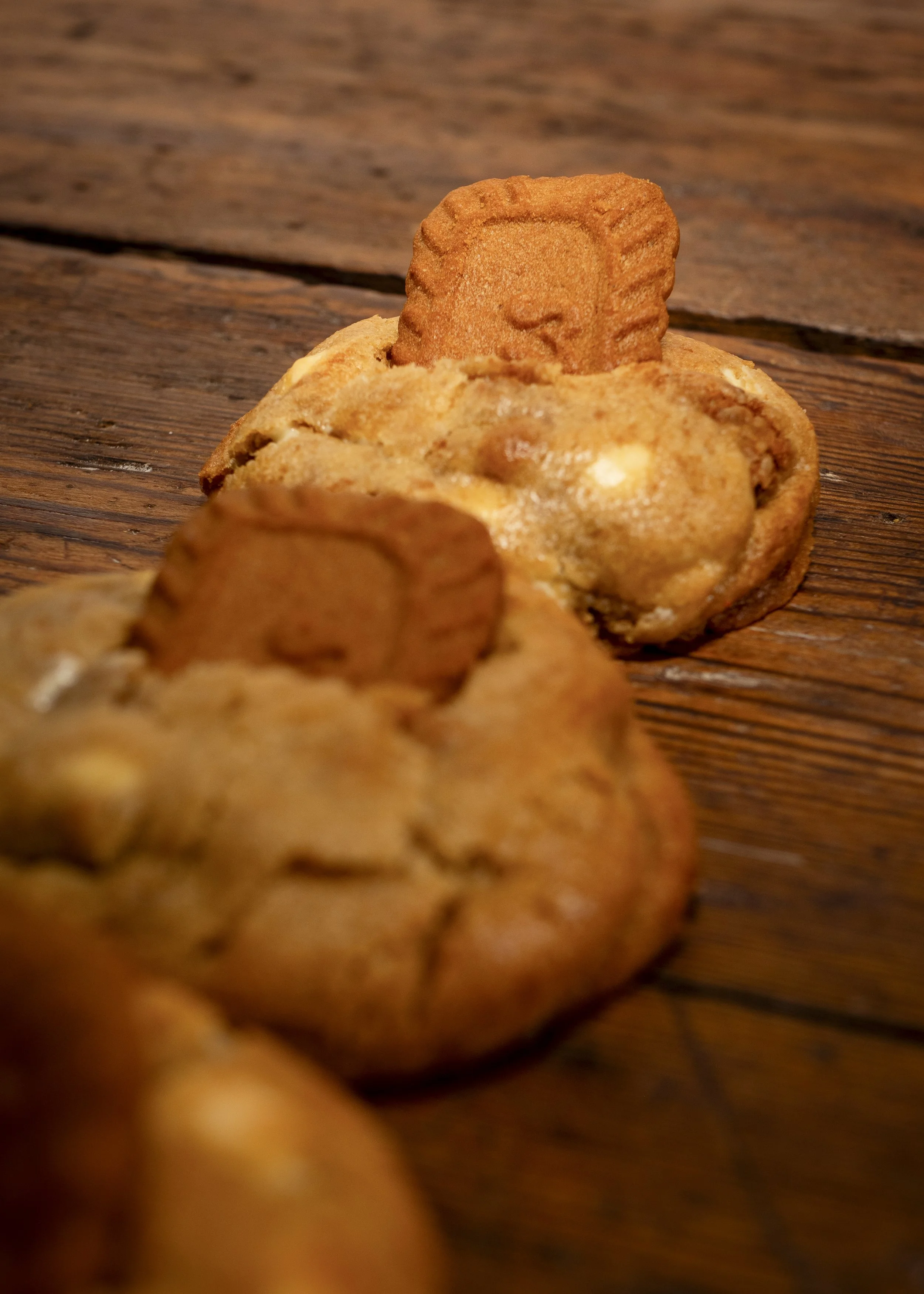 Close-up of chocolate chip cookies with a rectangular cookie at the top of each cookie, on a wooden surface.