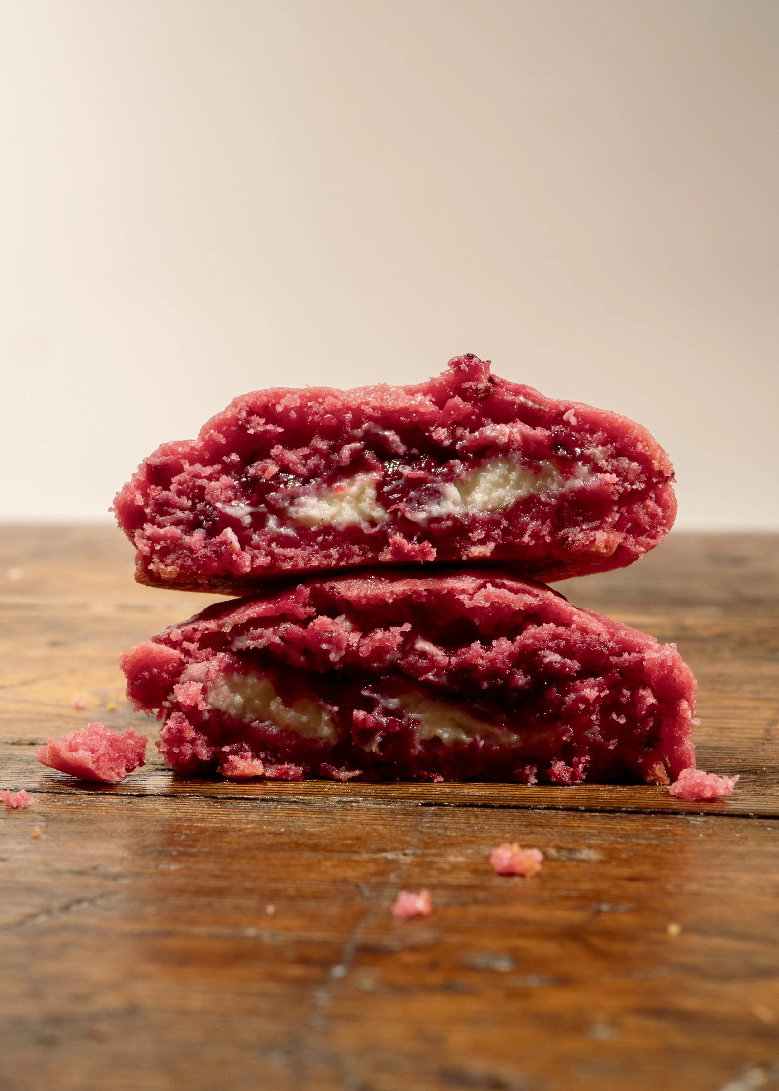 Two halved red cookies with cream and jam filling on a wooden surface.