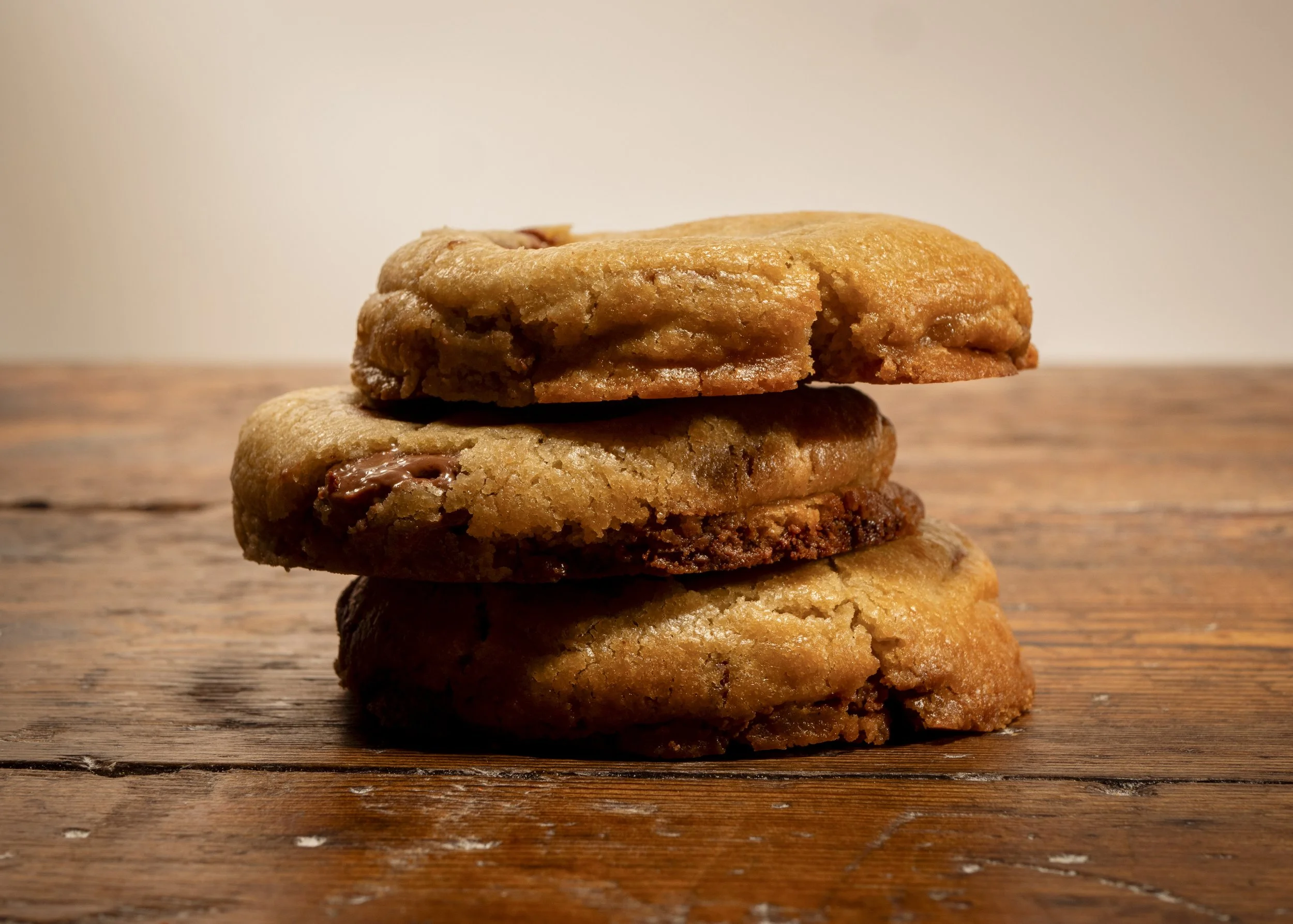 Stack of three chocolate chip cookies on a wooden surface.