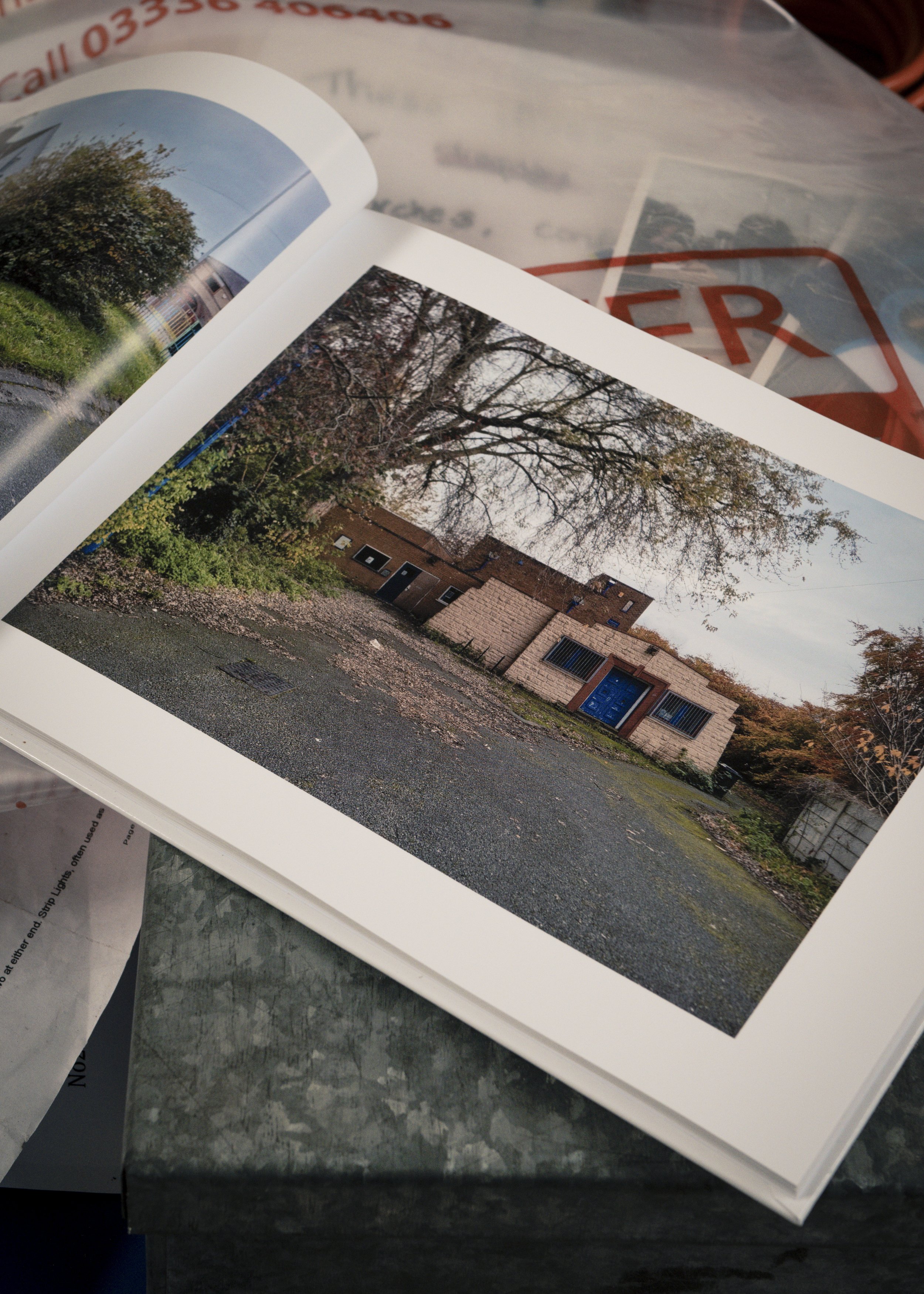 A photo album open to a picture of a small brick building with a blue door, surrounded by trees with some leaves fallen on the ground.