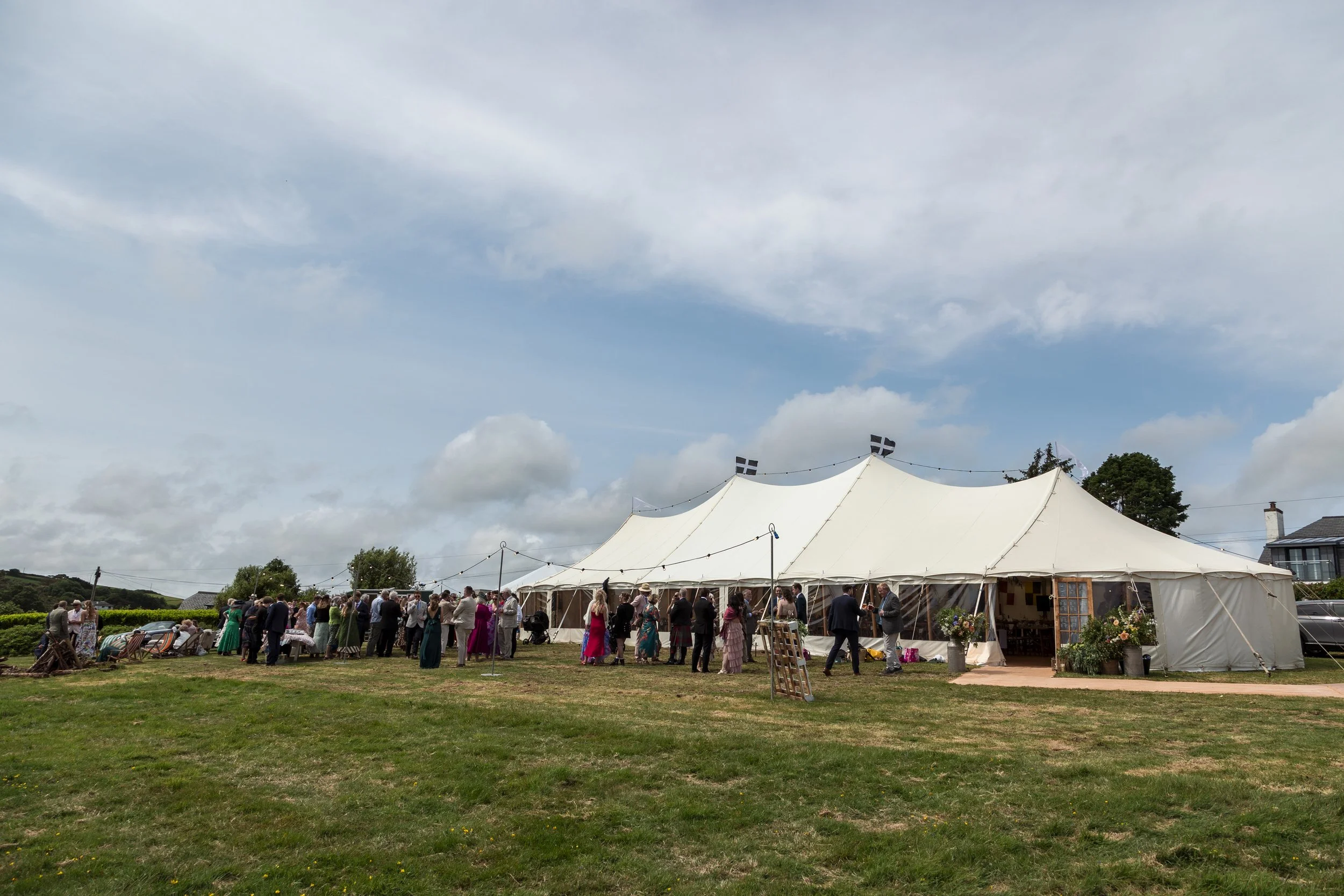 People gathering outside a large white tent under a partly cloudy sky during a daytime event.