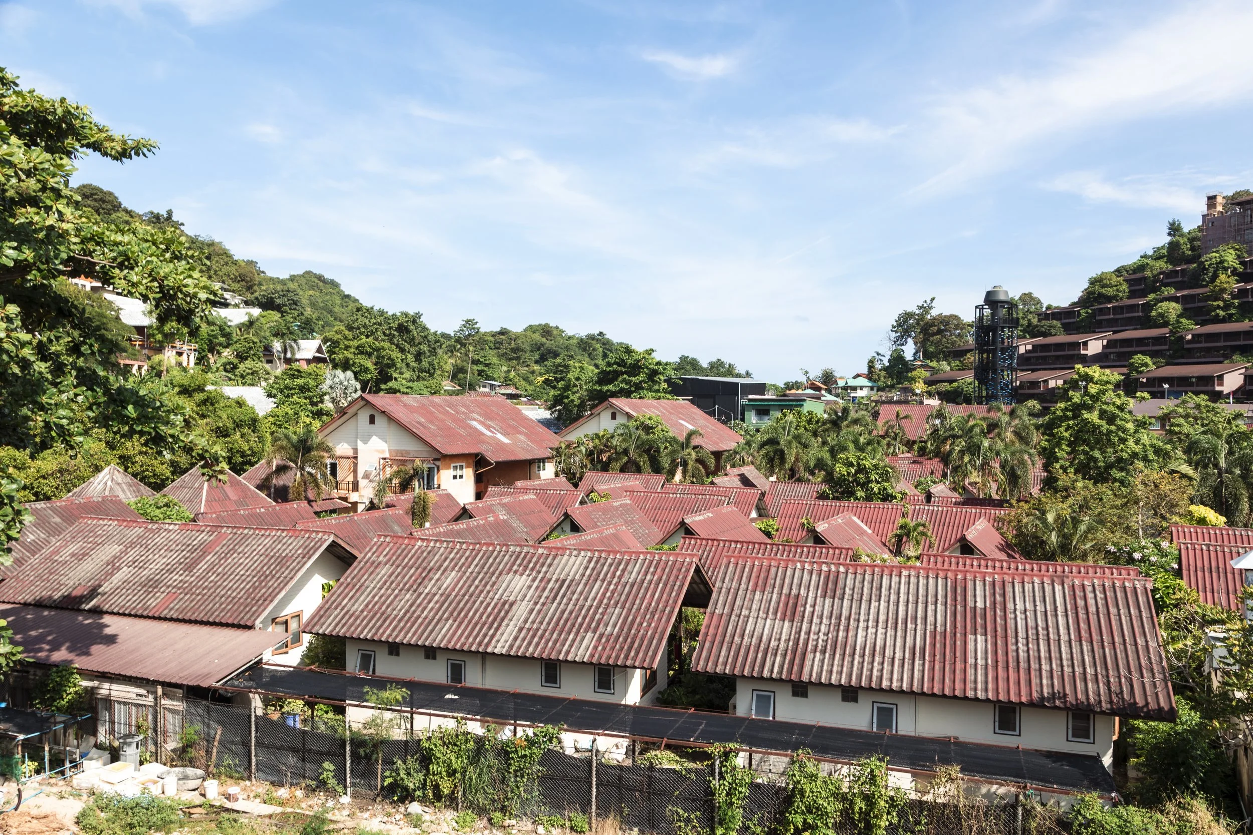 A hillside town with red-roofed houses, lush green vegetation, and a clear blue sky.