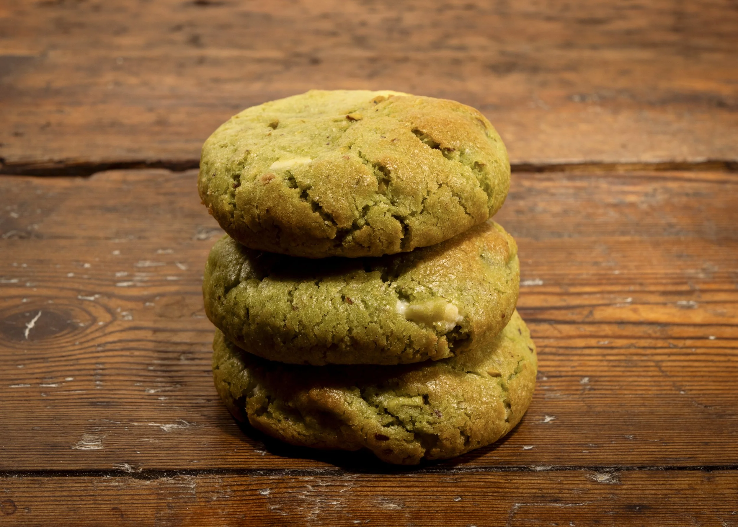Three green cookies stacked on a wooden surface.