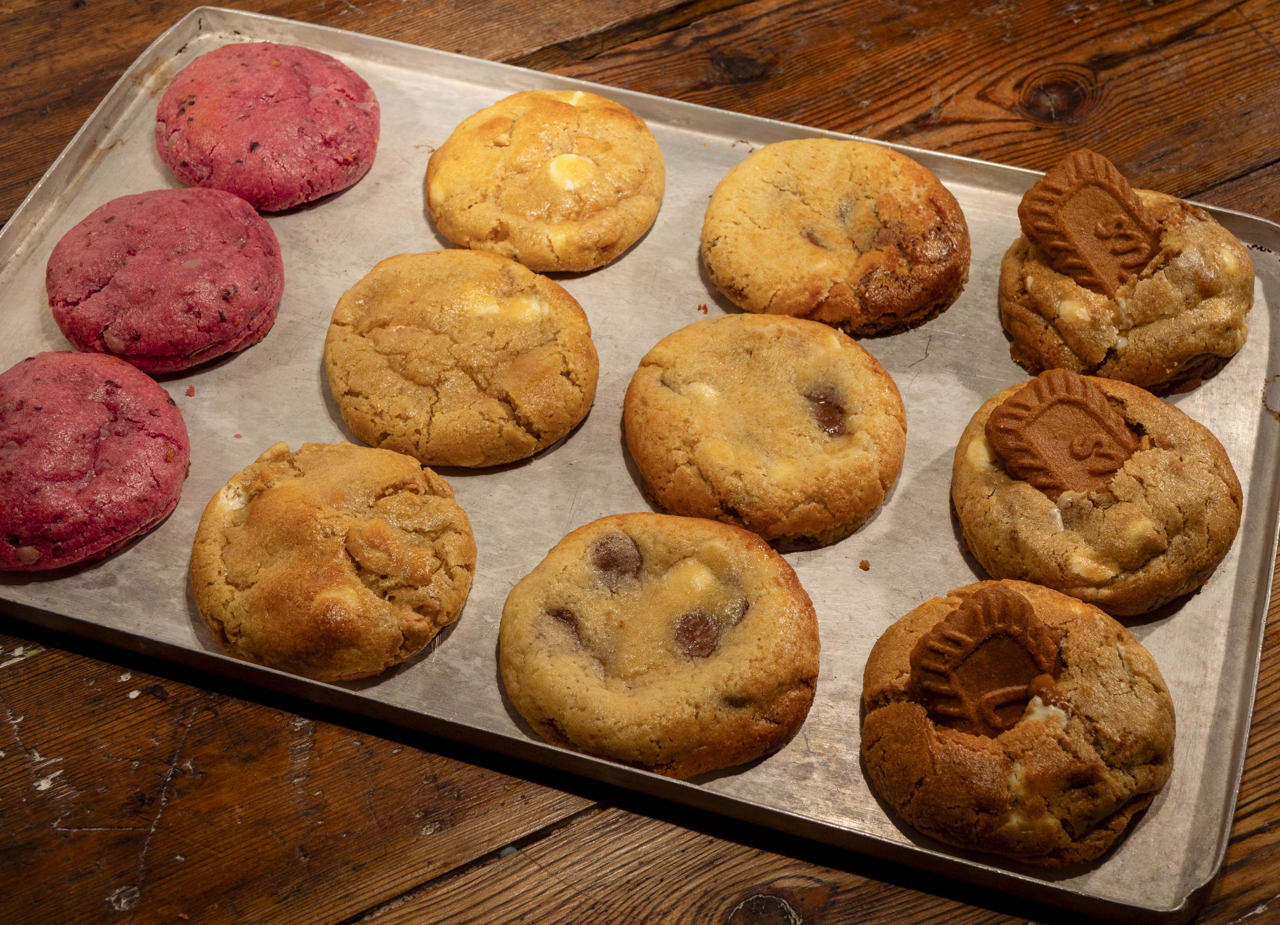 Tray of assorted cookies on parchment paper, including chocolate chip, peanut butter, and sugar cookies, on a wooden table.