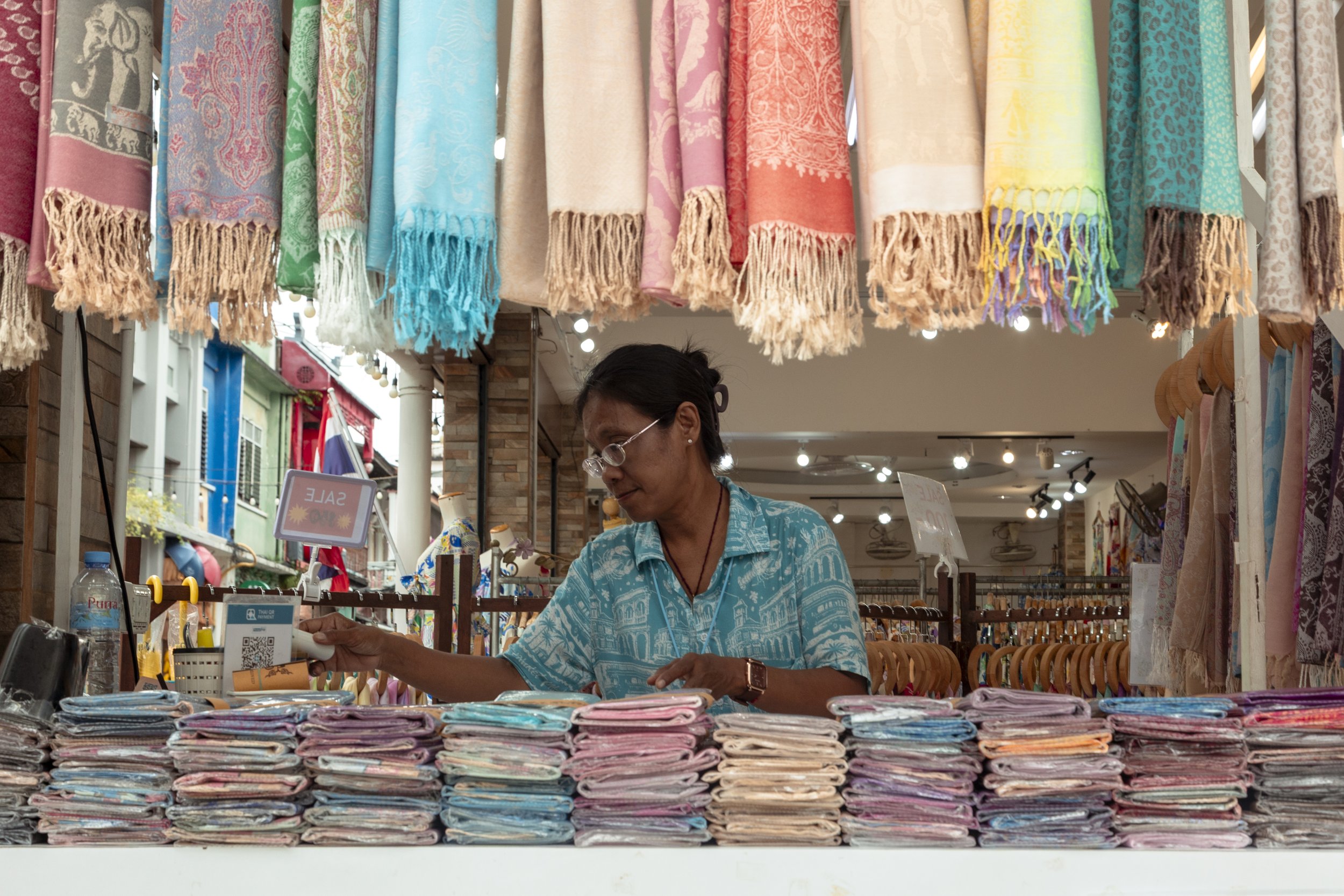 A woman sells colorful beach towels at an outdoor market stall.