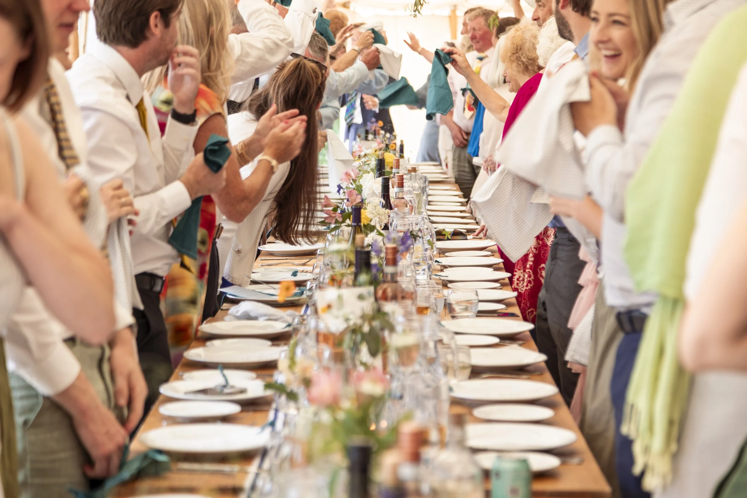 People are standing around a long, decorated dinner table, raising their glasses in a toast, in a festive indoor celebration.