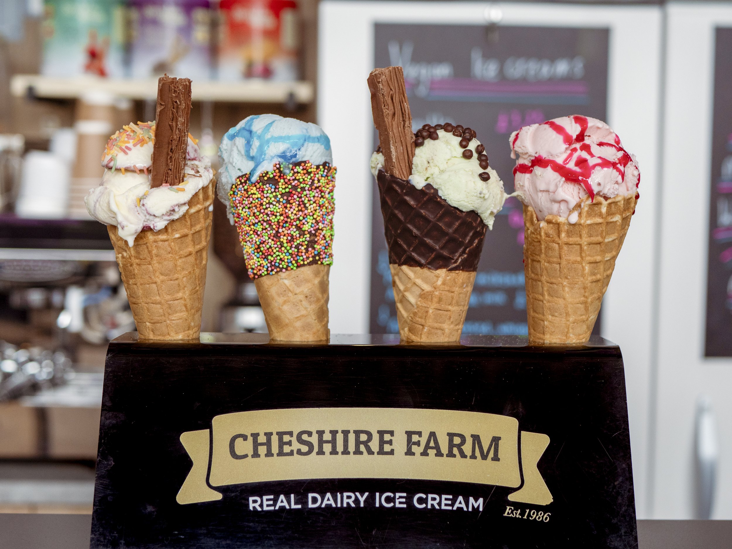 Four ice cream cones with various flavors and toppings displayed on a stand at Cheshire Farm ice cream shop.