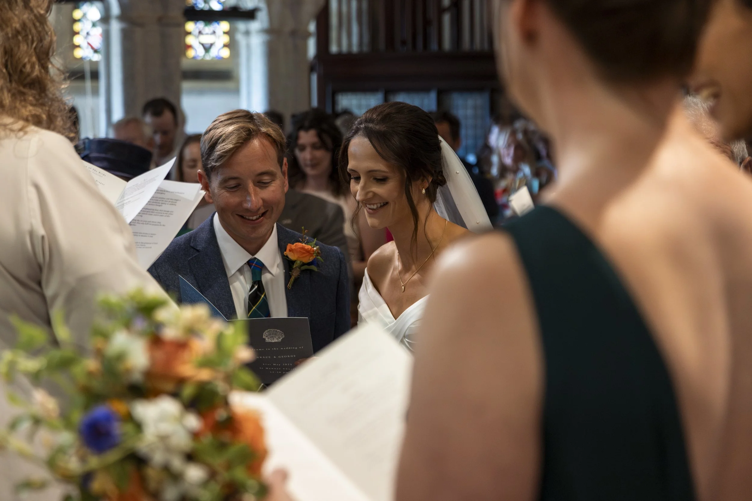 A wedding ceremony with a couple exchanging vows, surrounded by friends and family inside a church with stained glass windows.