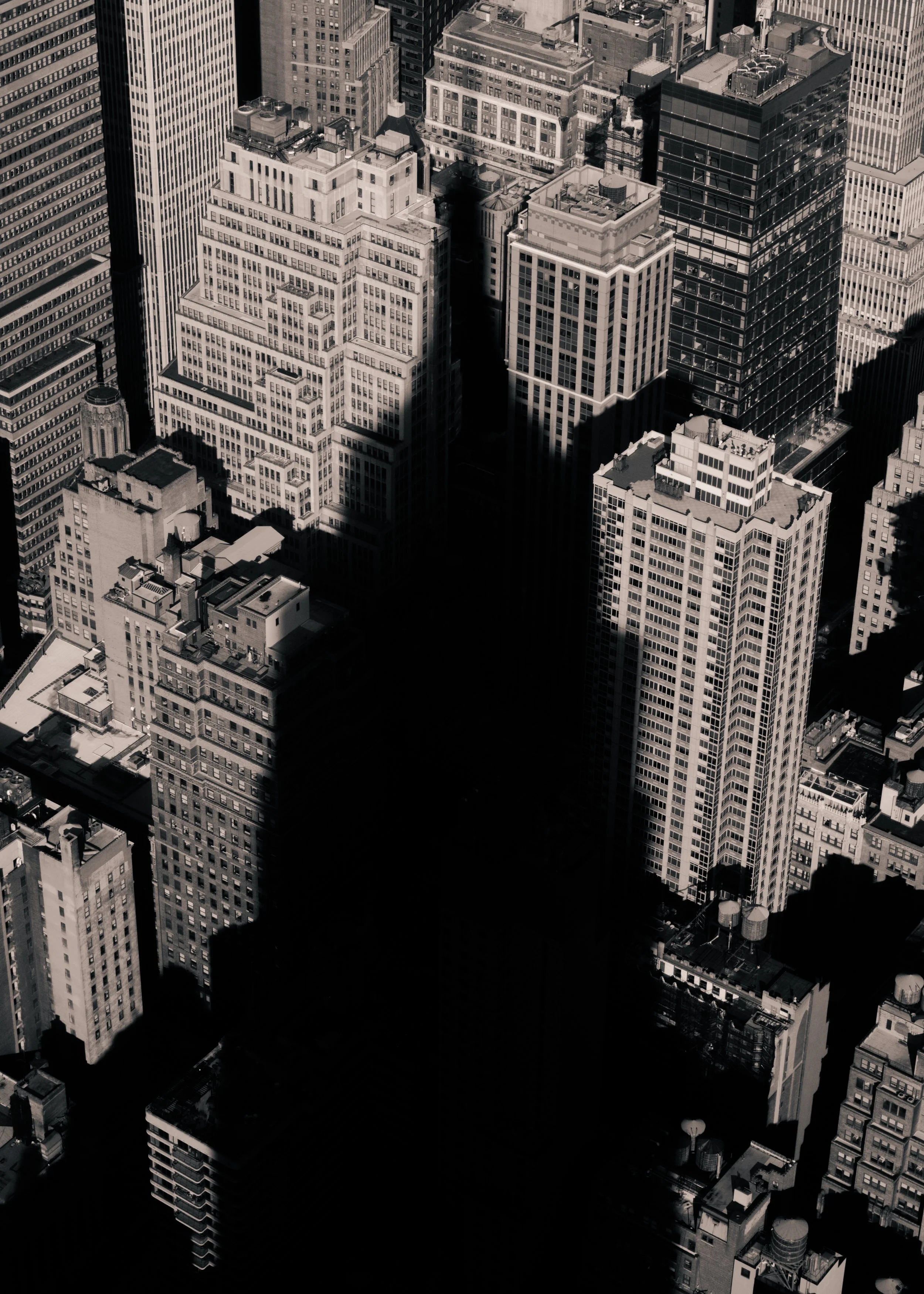 Black and white aerial view of skyscrapers in a city, with a tall shadow cast across the buildings.