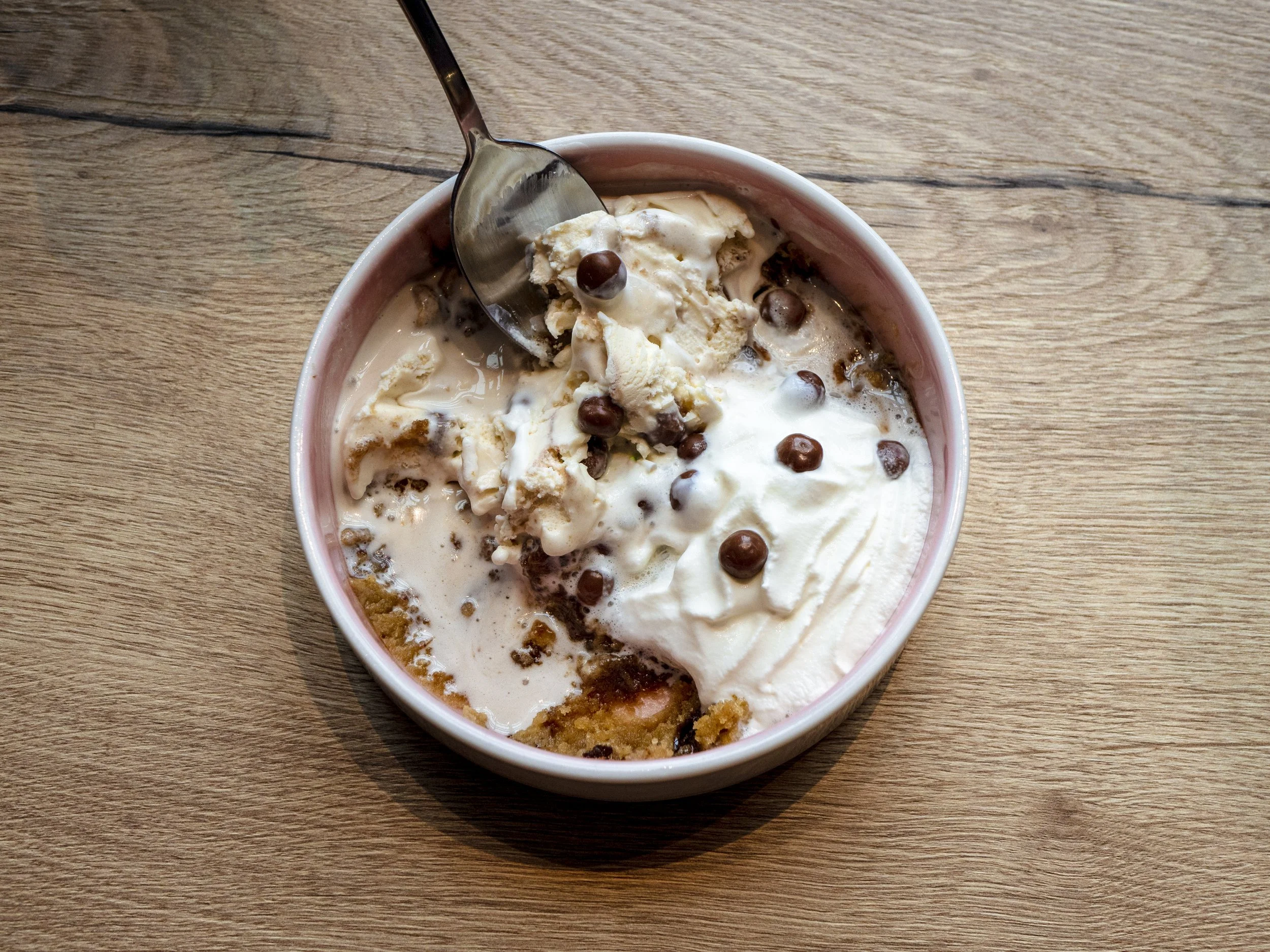 A bowl of ice cream topped with chocolate chips, served with a spoon on a wooden table.
