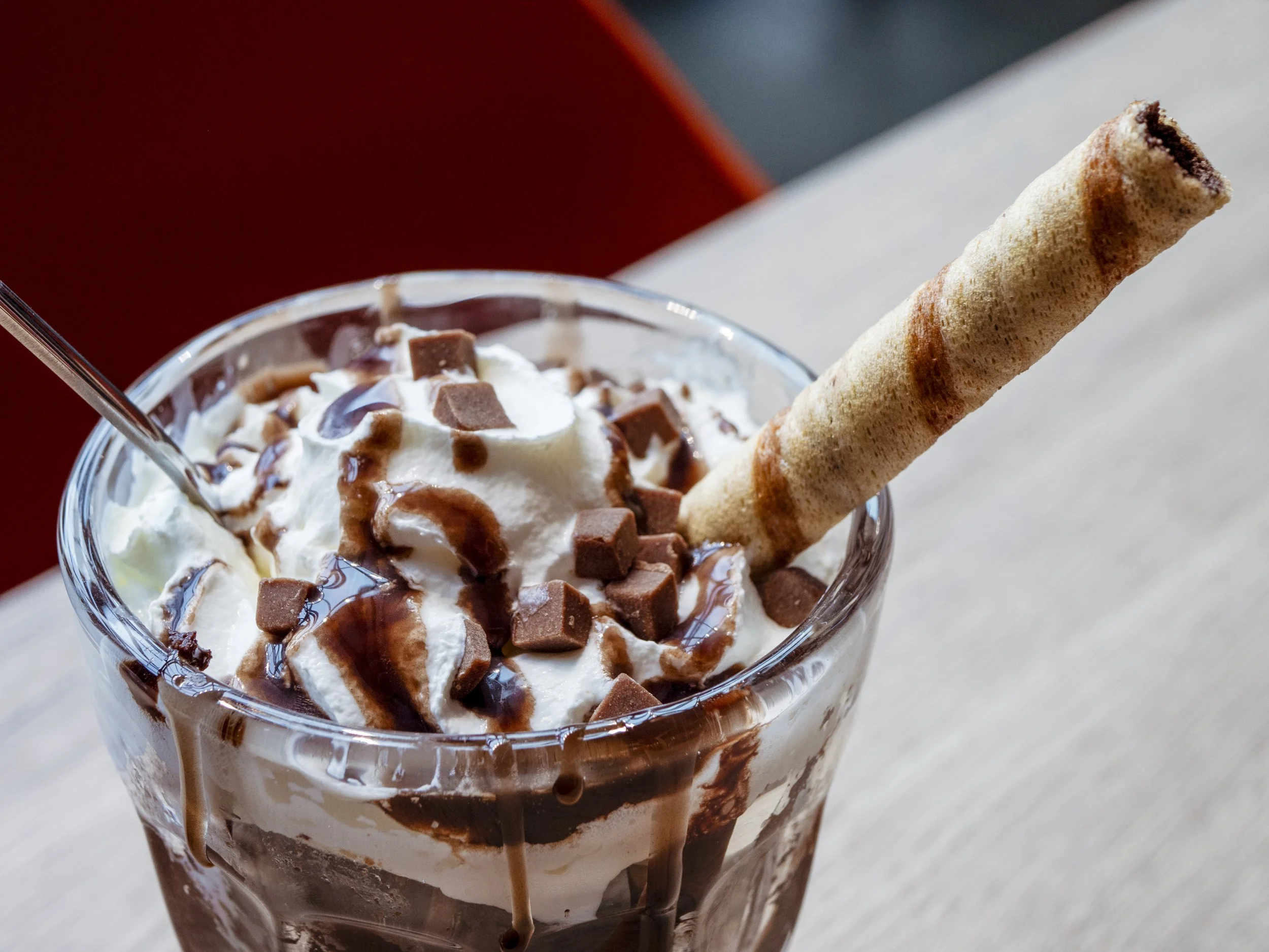 A glass of chocolate sundae with whipped cream, chocolate syrup, chocolate chunks, and a wafer roll on top.