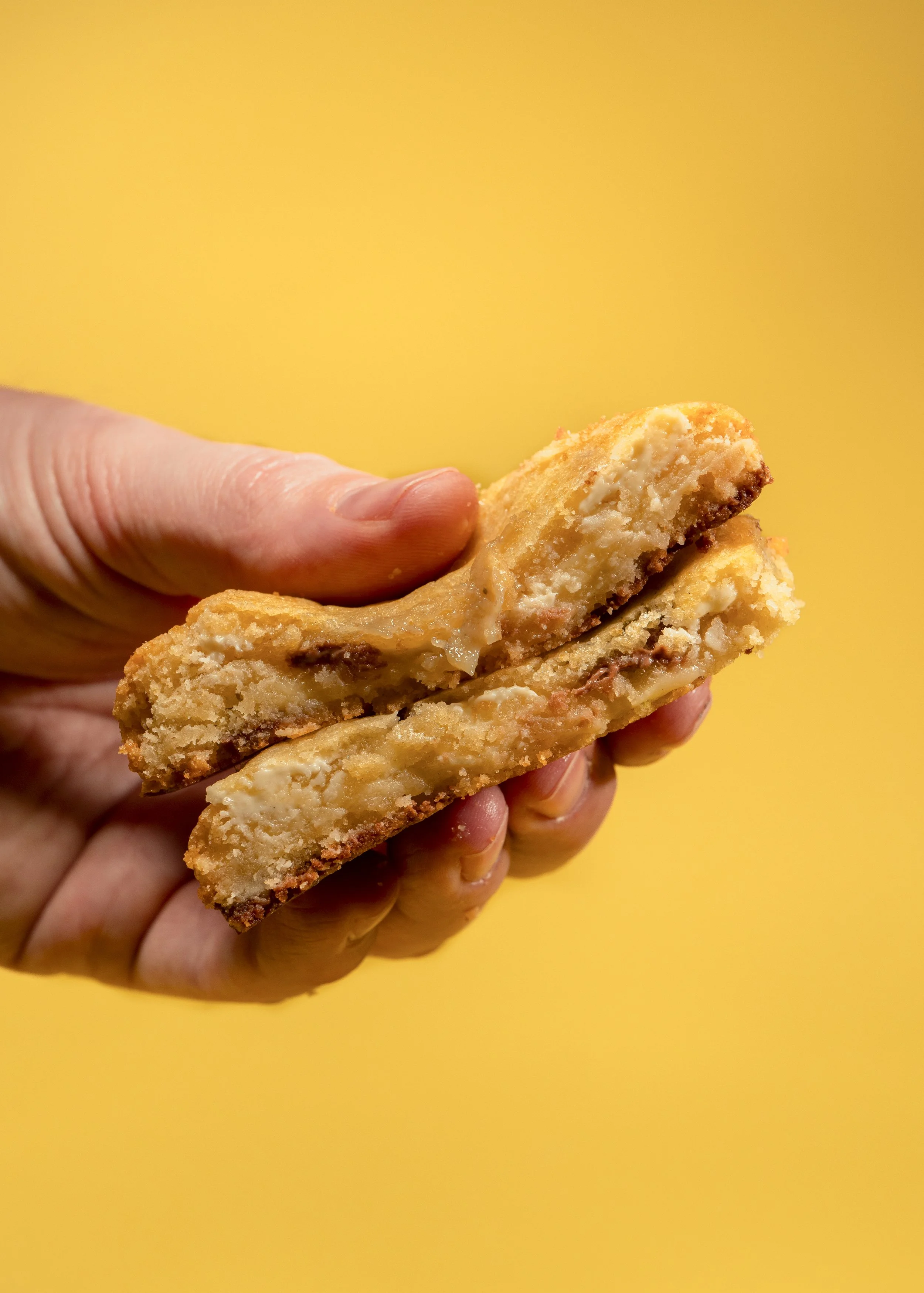 Close-up of a hand holding two pieces of a homemade apple cinnamon dessert bar against a yellow background.