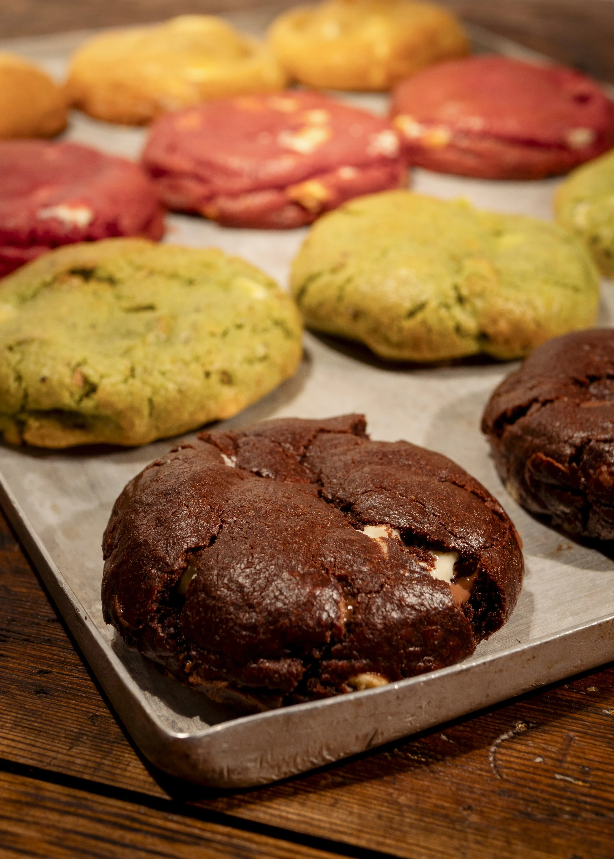 A tray of assorted cookies with different colors and textures, including chocolate, green, yellow, and red cookies.