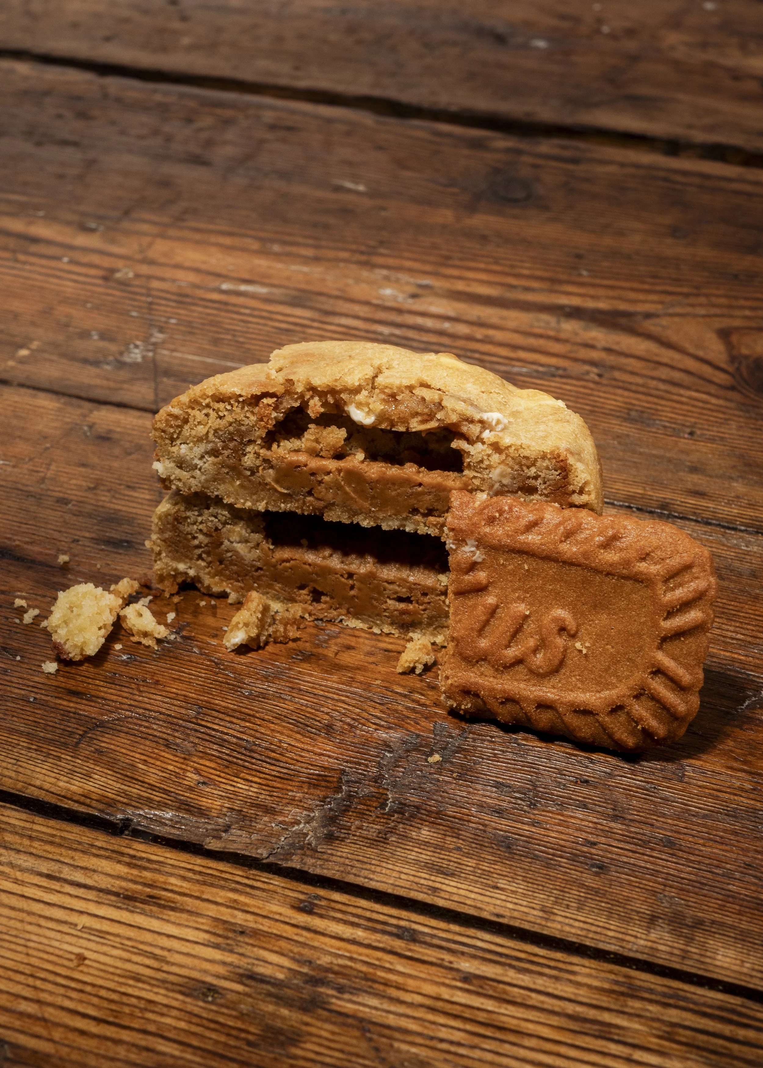 A partially eaten peanut butter cookie with a stamped 'S' on it, placed on a rustic wooden surface, with cookie crumbs around.