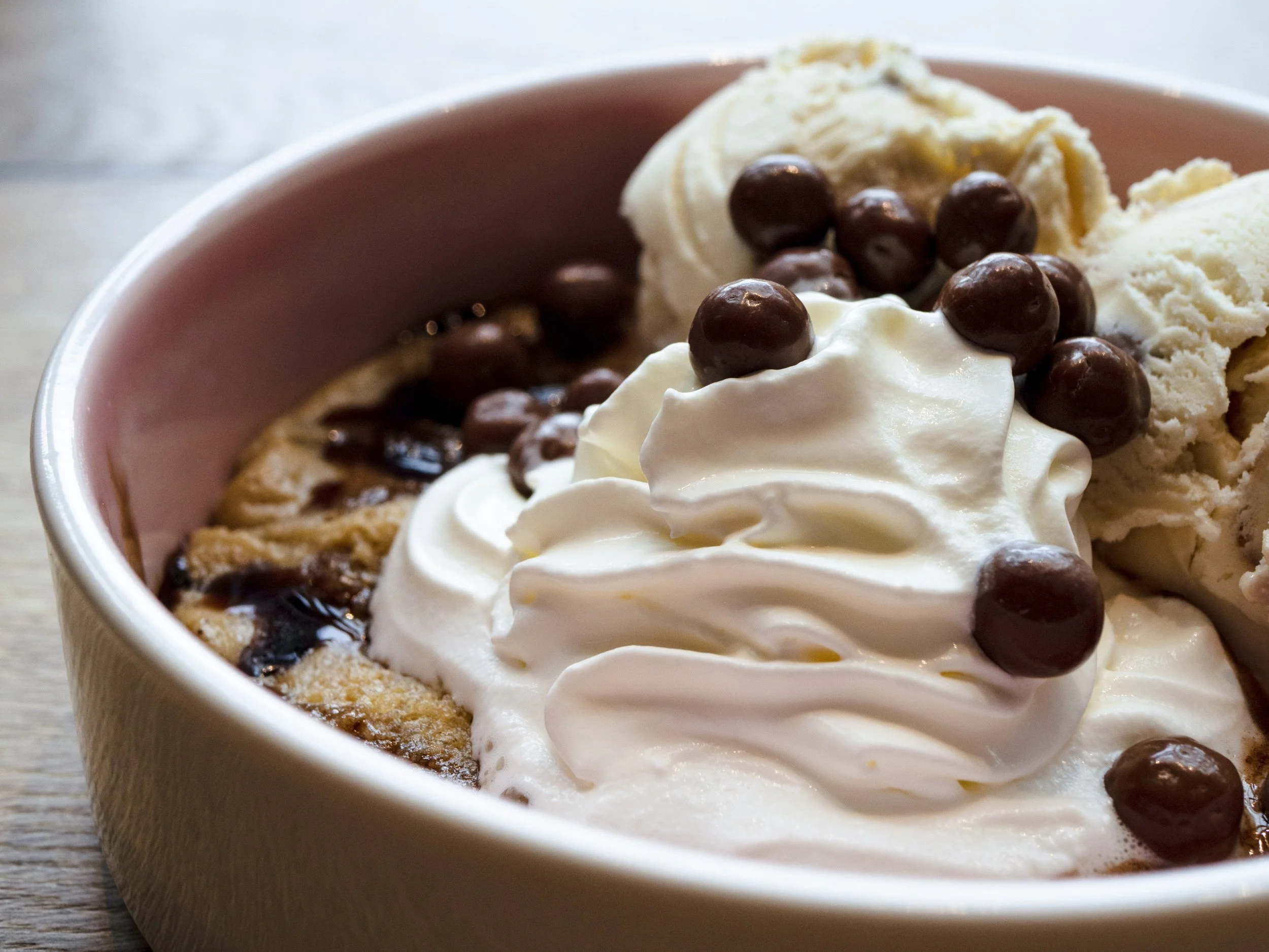 Chocolate chip cookie sundae with whipped cream and chocolate-covered peanuts in a pink bowl.