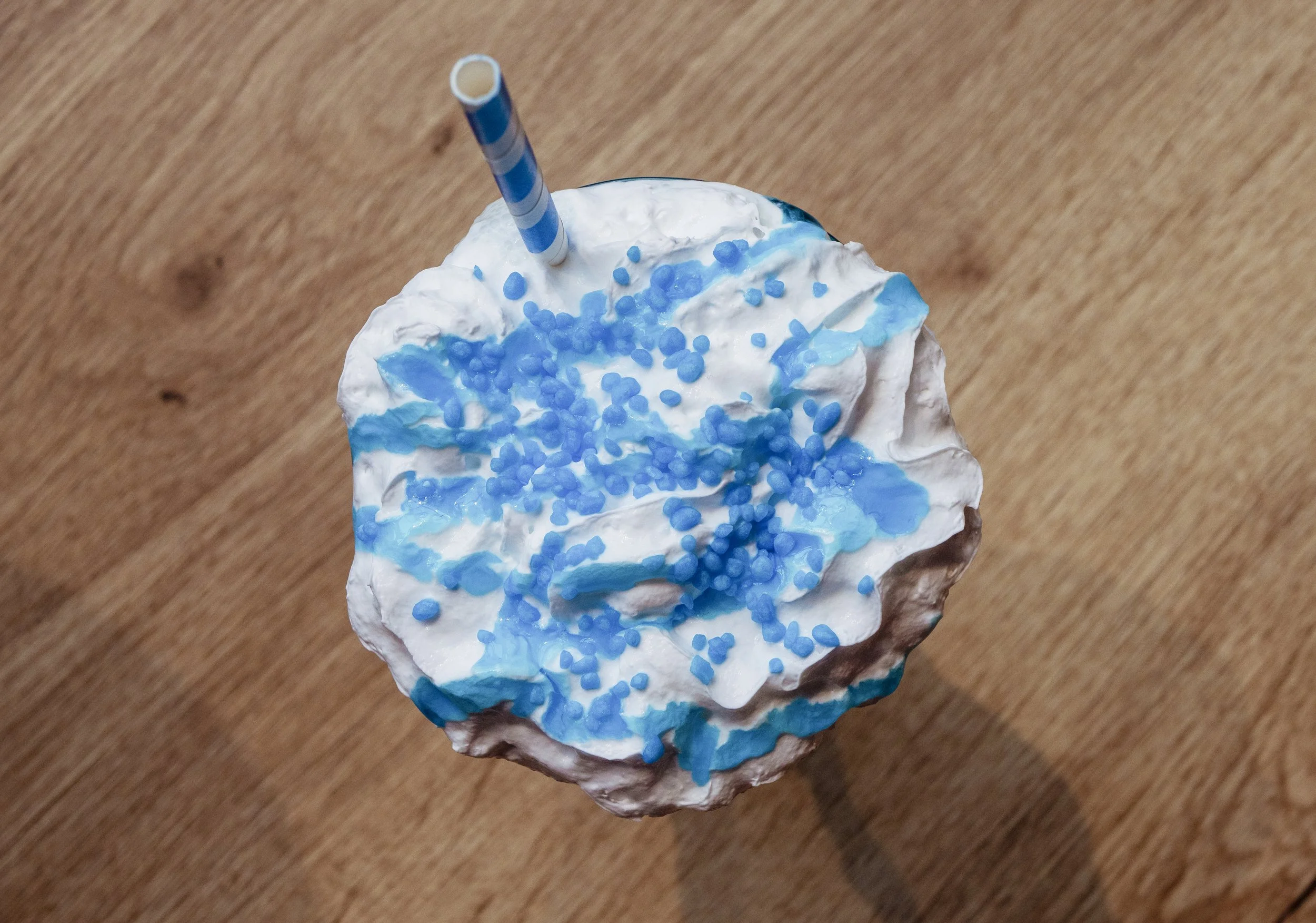 Whipped cream topping with blue sprinkles and a blue-striped straw on a wooden surface.
