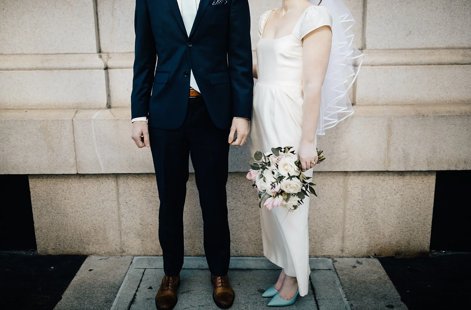 A Raleigh couple stands with a pastel spring bridal bouquet outside the downtown Raleigh, NC courthouse after a microwedding ceremony
