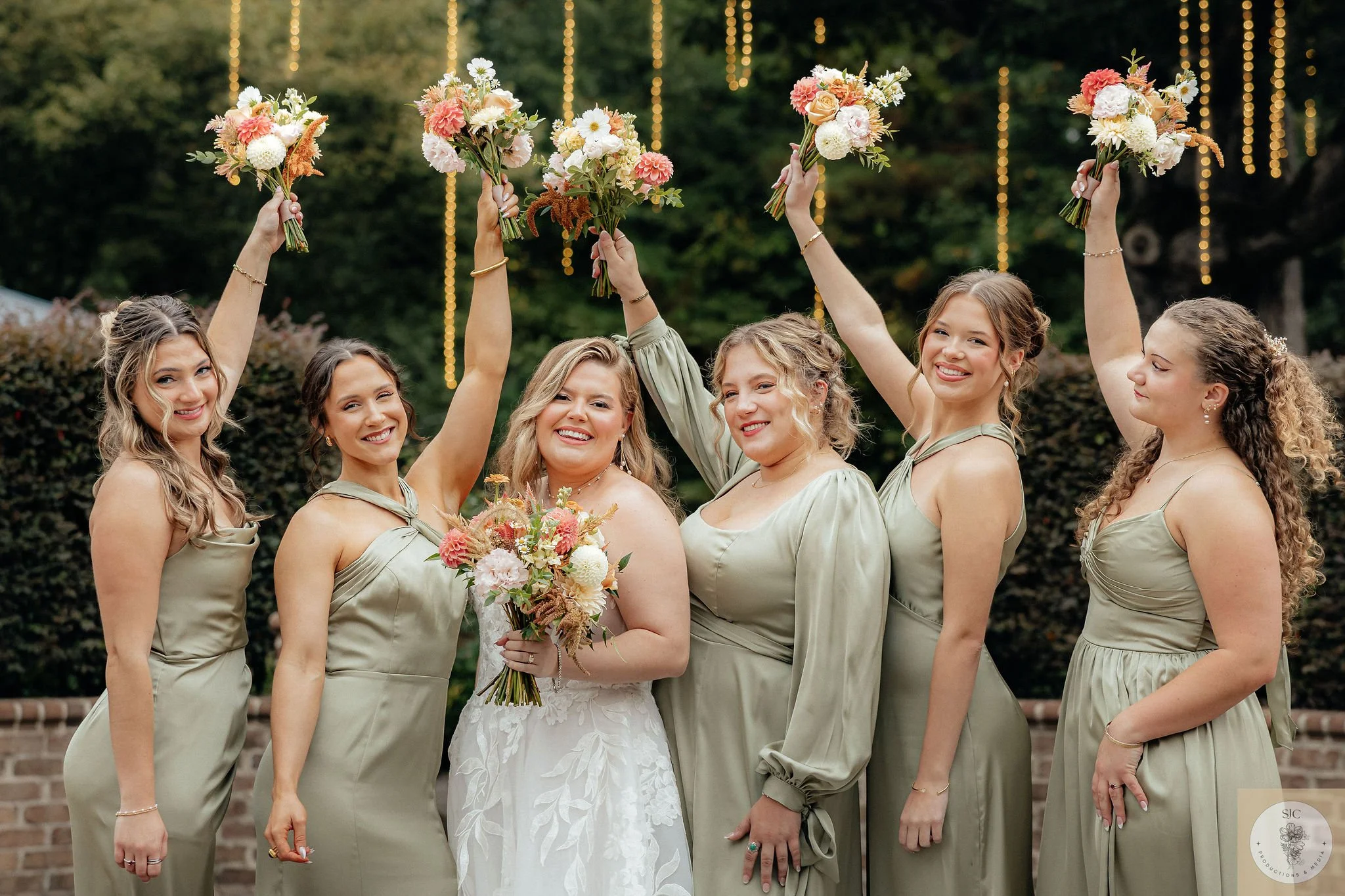 Bridesmaids in sage green dresses hold fall wedding flowers over a bride at the Sutherland in Raleigh, NC