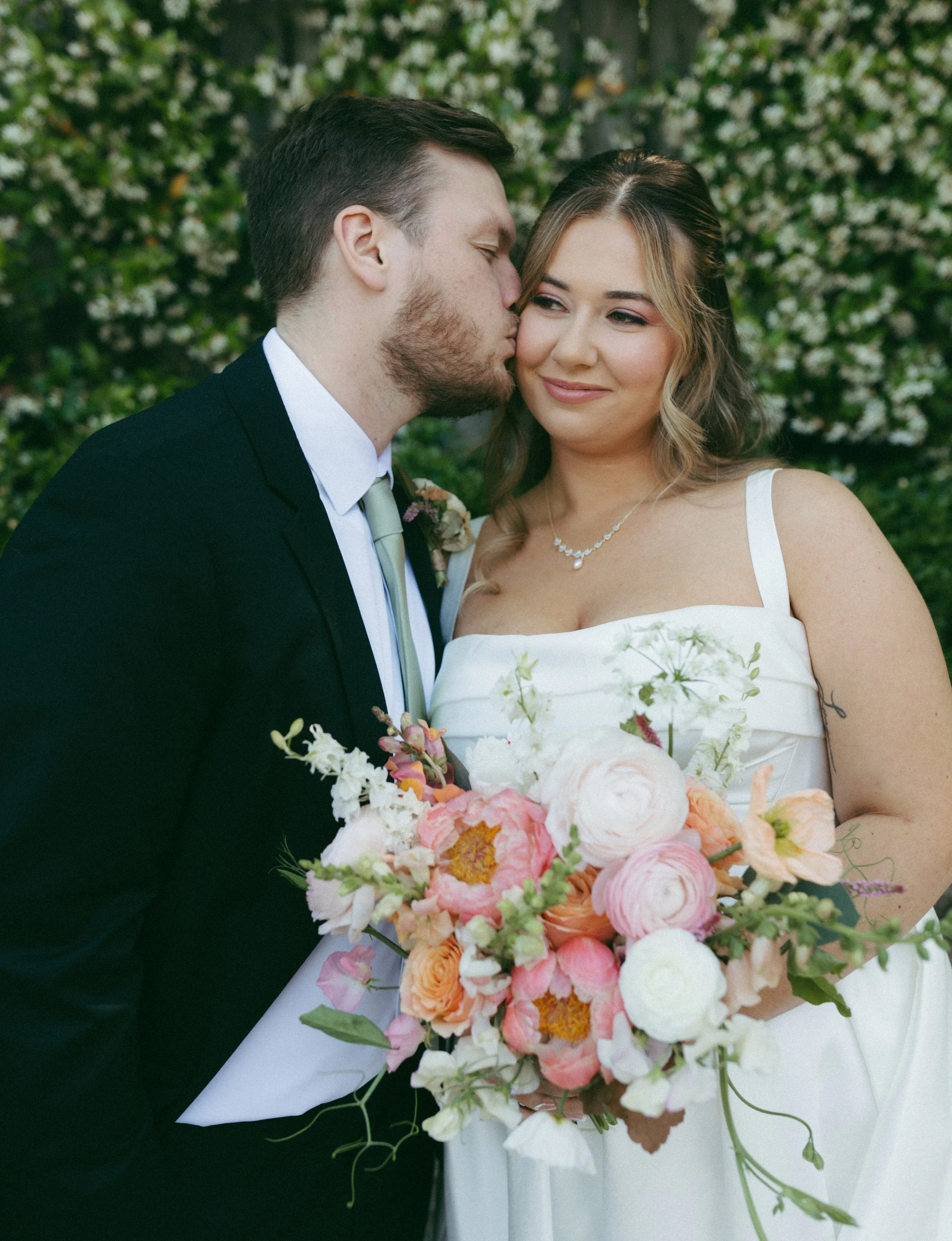 A bride and groom pose with a bright spring bridal bouquet at the cookery in durham, nc